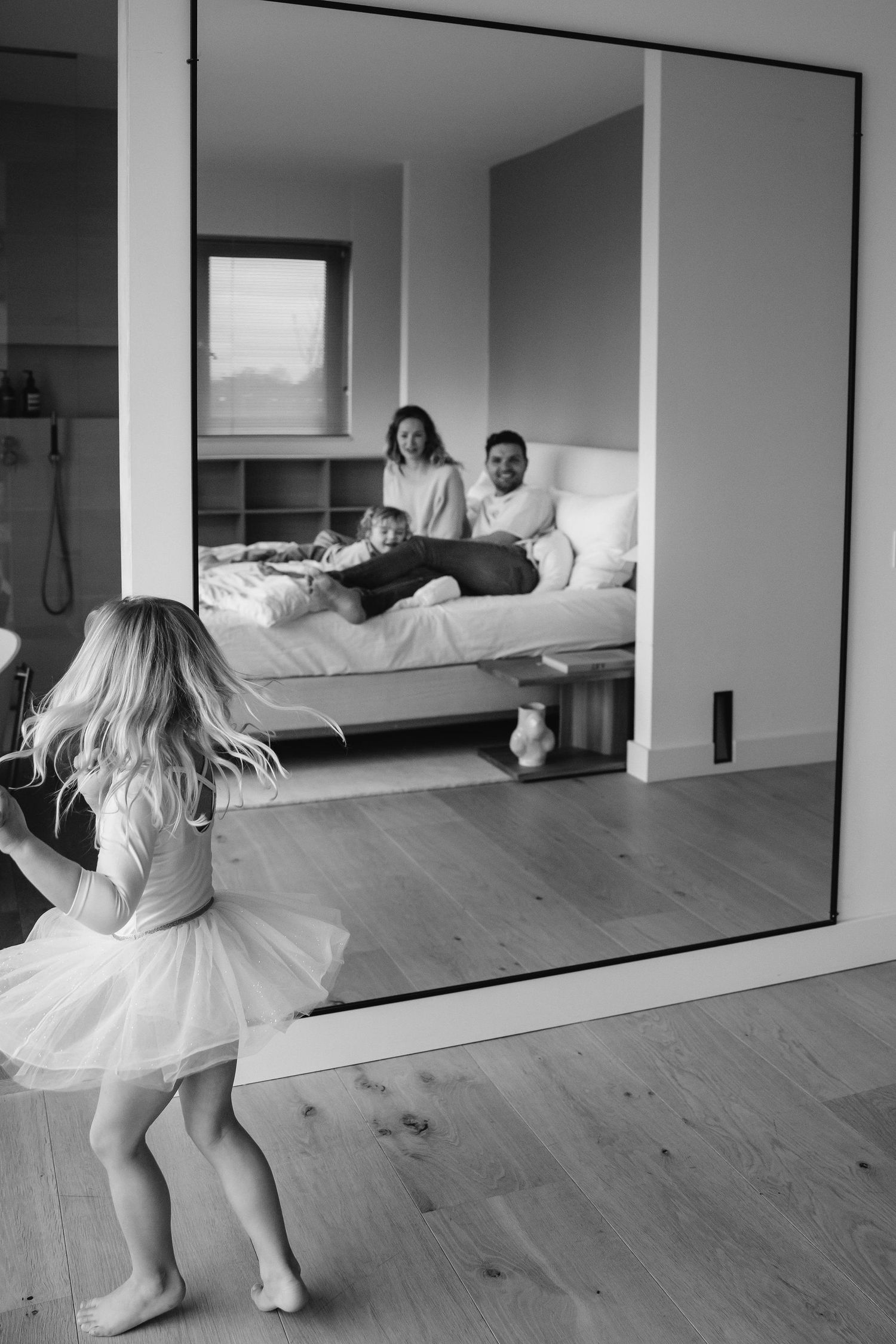 A black and white photo of a dancing child with a tulle skirt reflected in a large mirror.