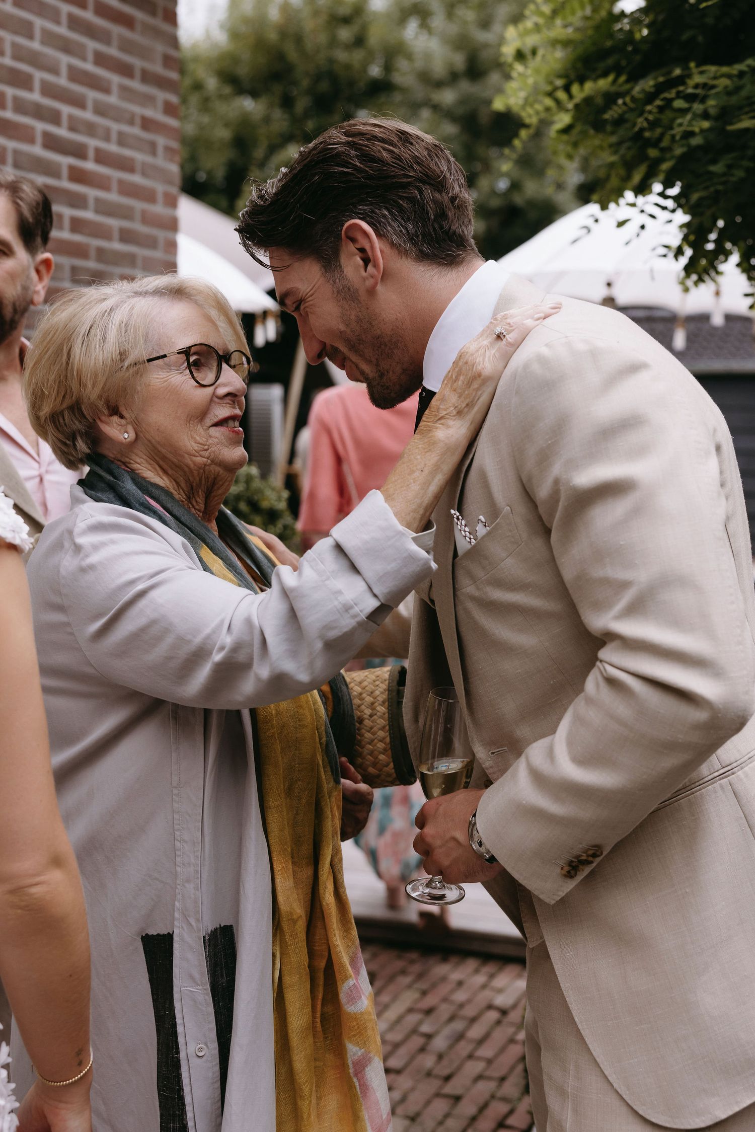 Emotional moment shared between a young man in beige suit and elderly woman.