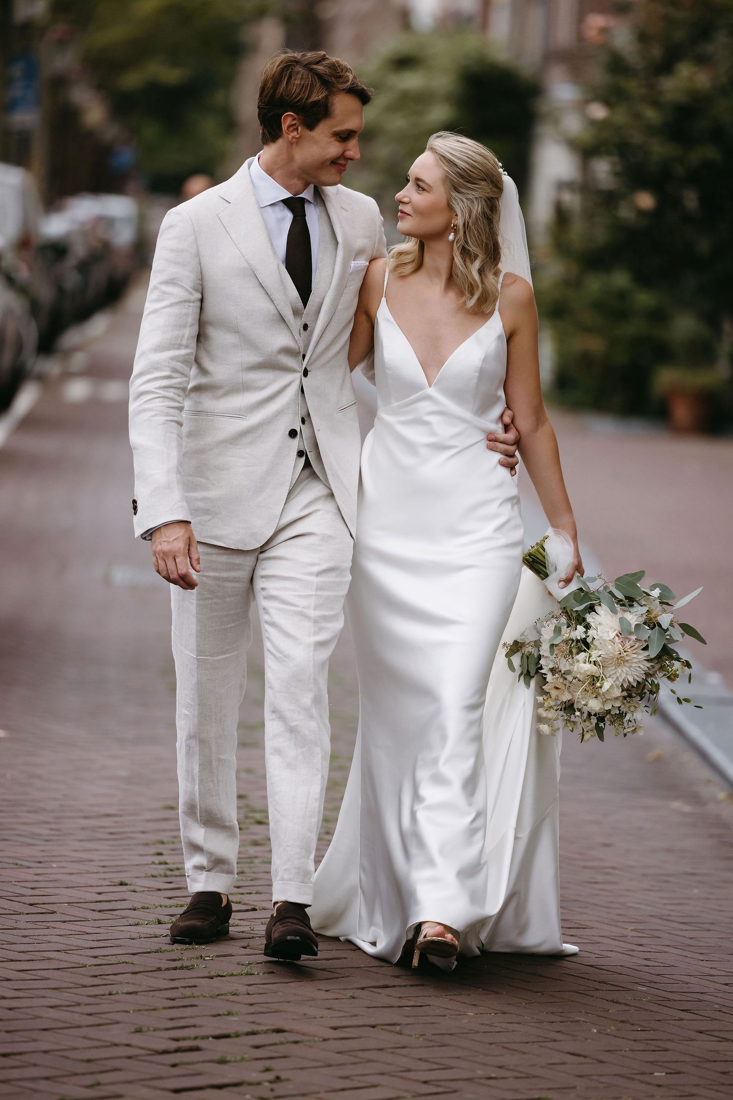 A couple in matching white outfits walking together on a brick street.