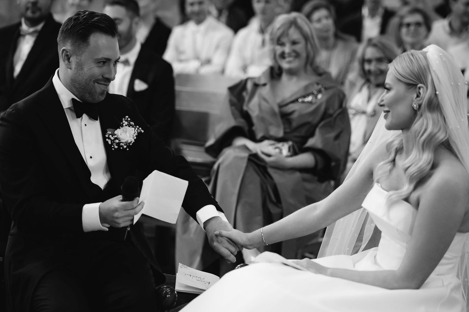 A black and white wedding ceremony photograph capturing an exchange of vows or rings.