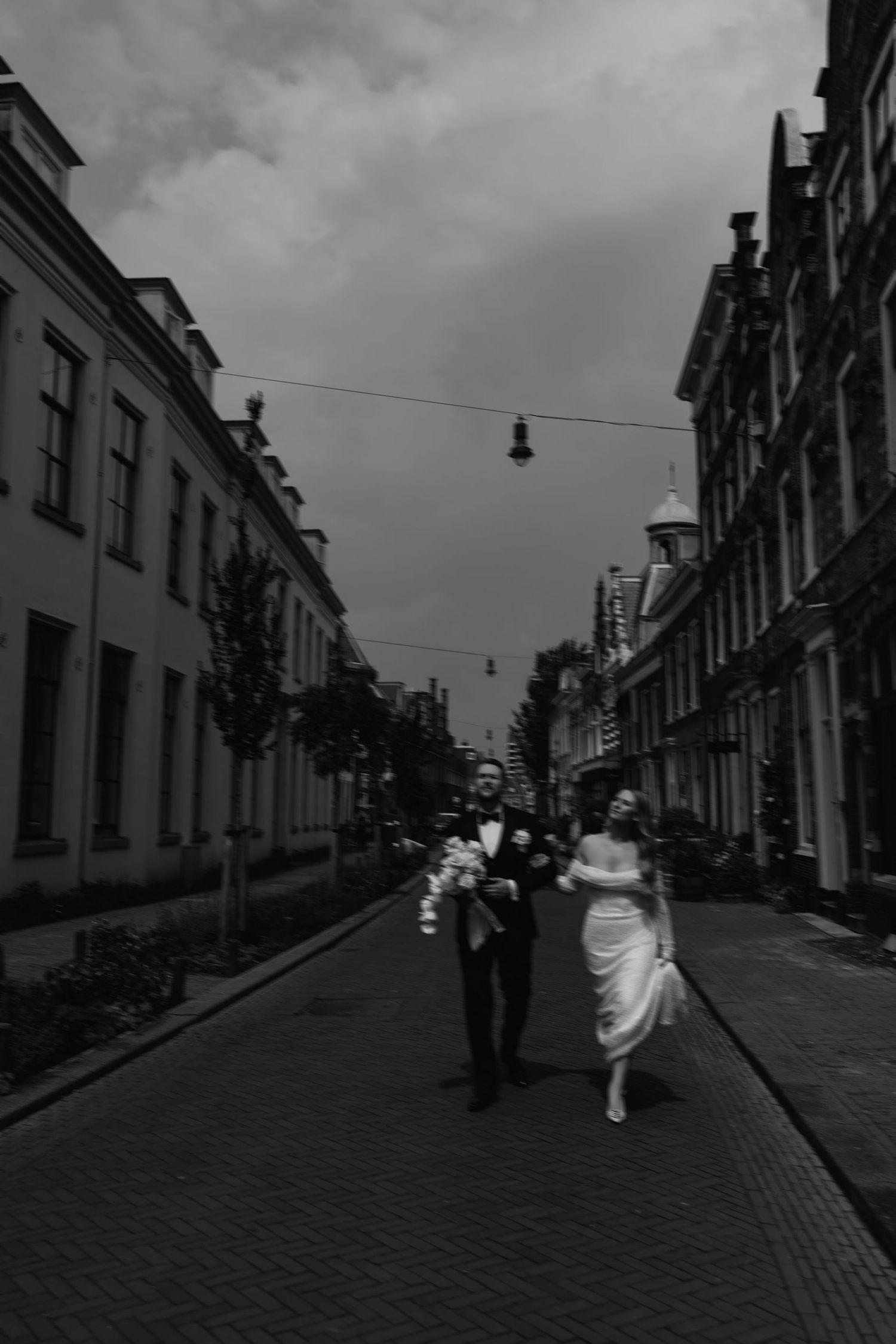A black and white photo of a couple walking down a cobblestone street with hanging lights above.