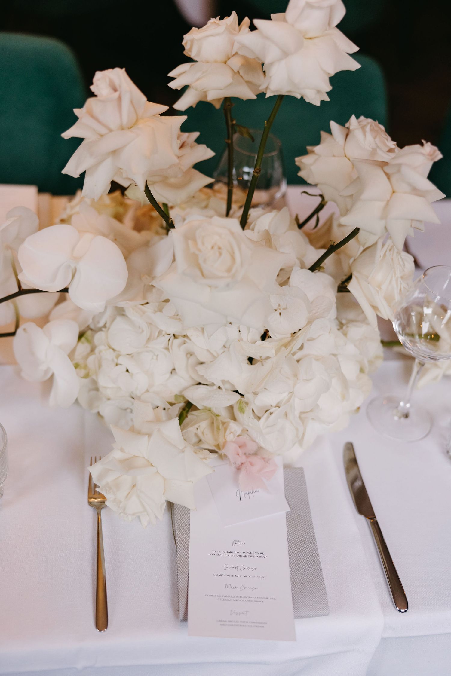 White rose and hydrangea centerpiece arrangement with menu card on elegant table setting.