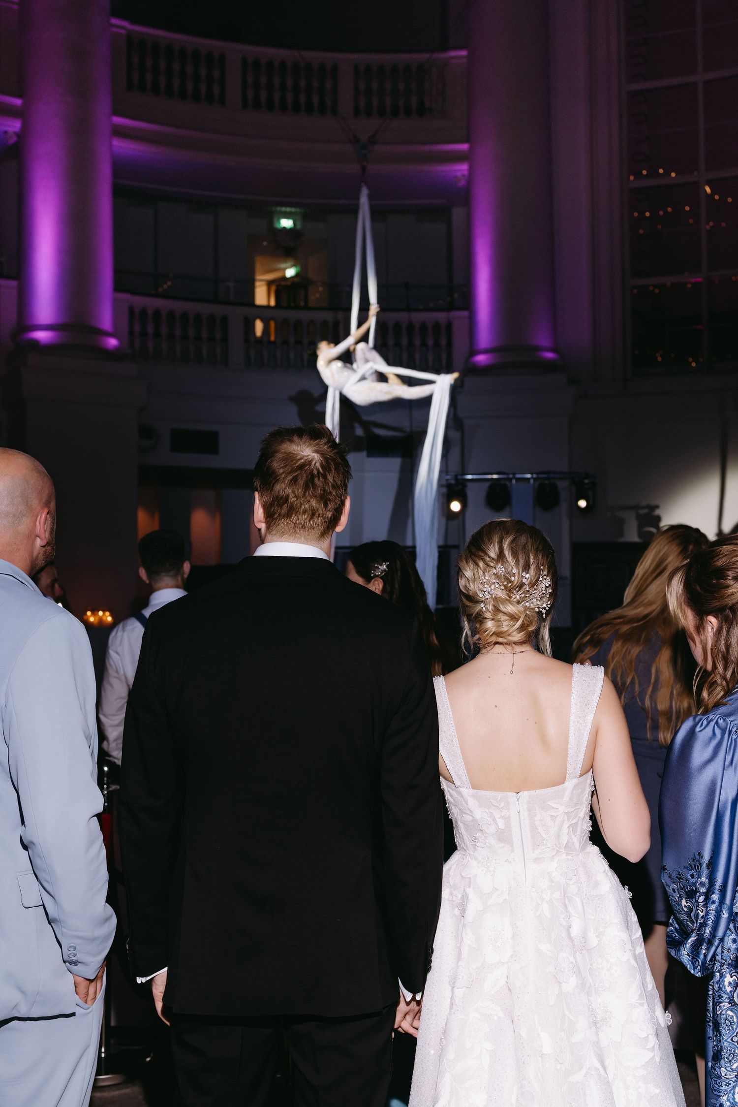 Wedding reception venue with purple accent lighting and guests mingling in formal attire.