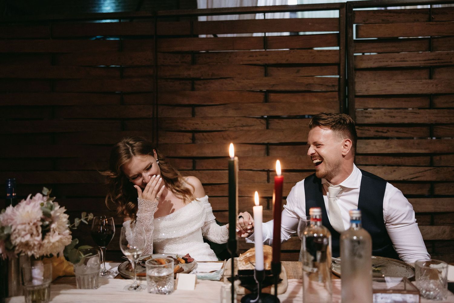 Intimate candlelit wedding reception dinner with elegant table settings and rustic wood walls.
