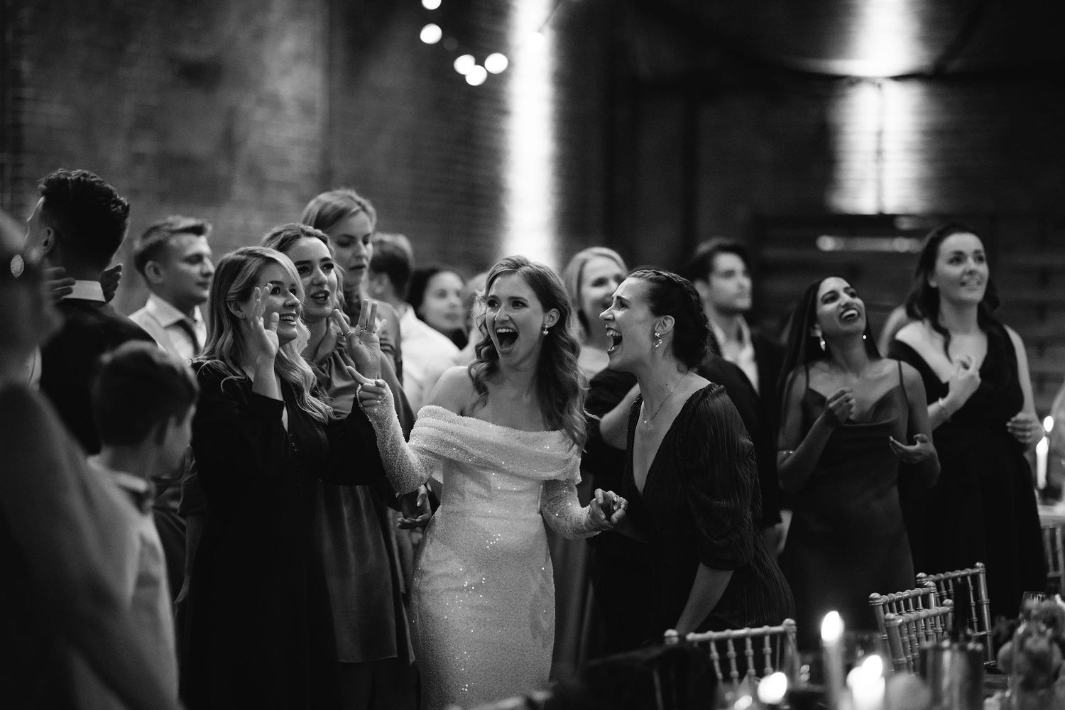 Wedding guests laugh joyfully during a candlelit reception celebration.