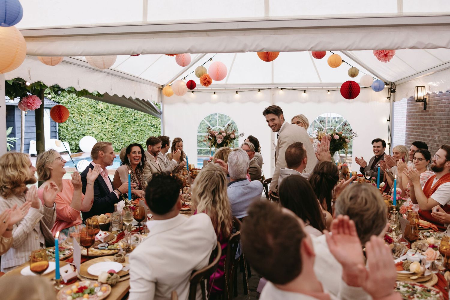 Outdoor wedding reception setup with orange and pink paper lanterns hanging above dining tables.