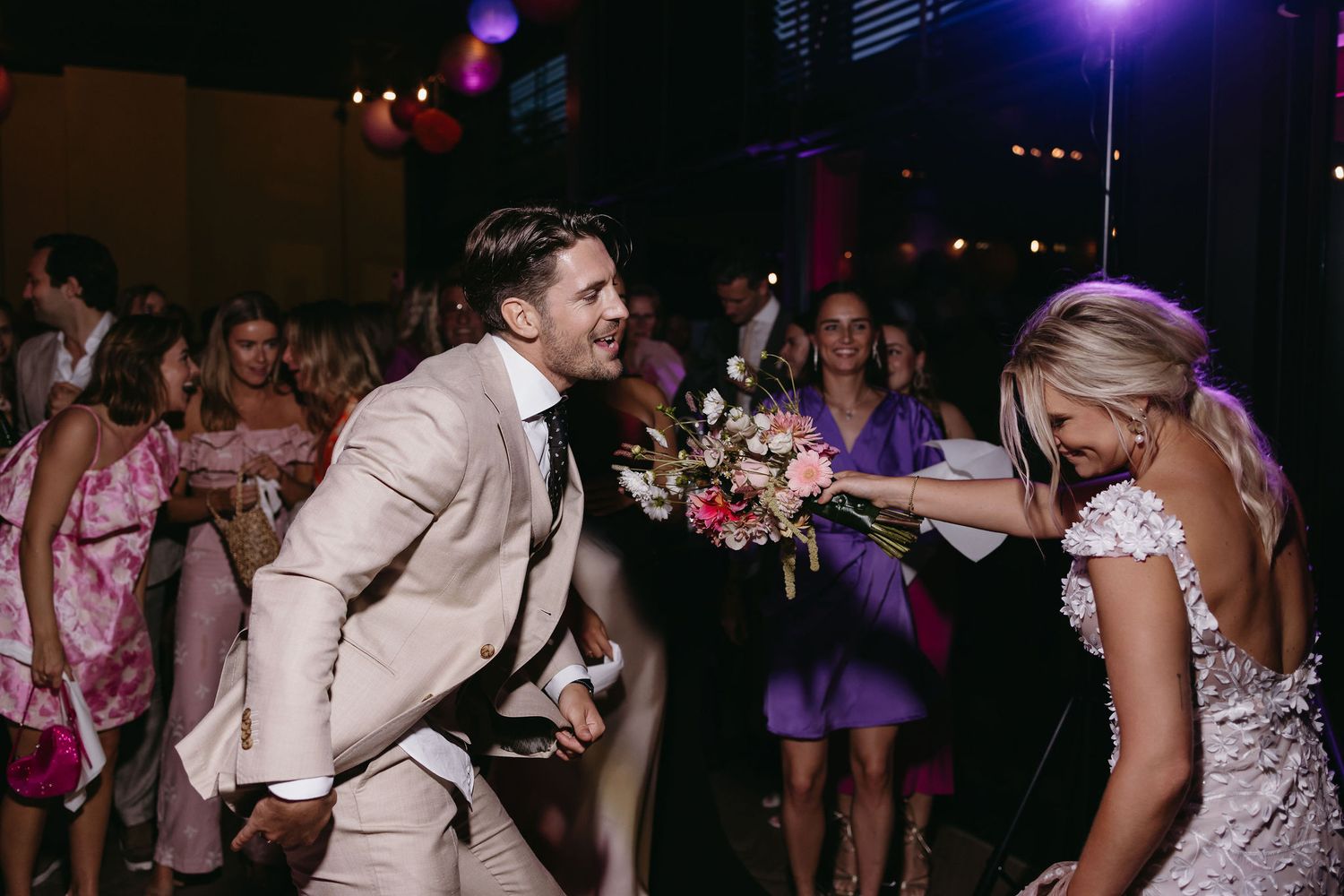 Dancing couple sharing joyful moment at wedding reception with guests in background.