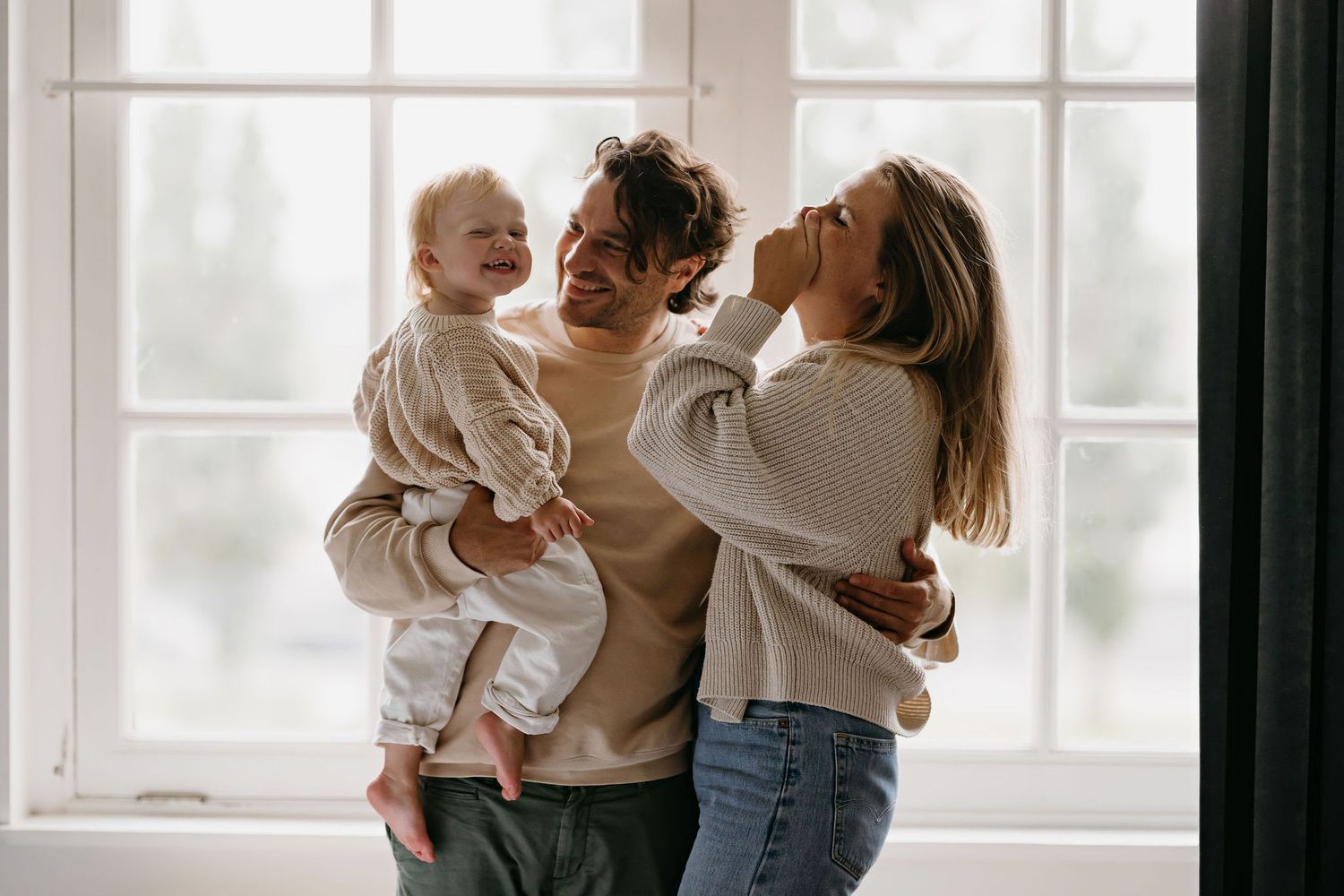 A family shares a joyful moment together by a bright window in their home wearing cozy casual attire.