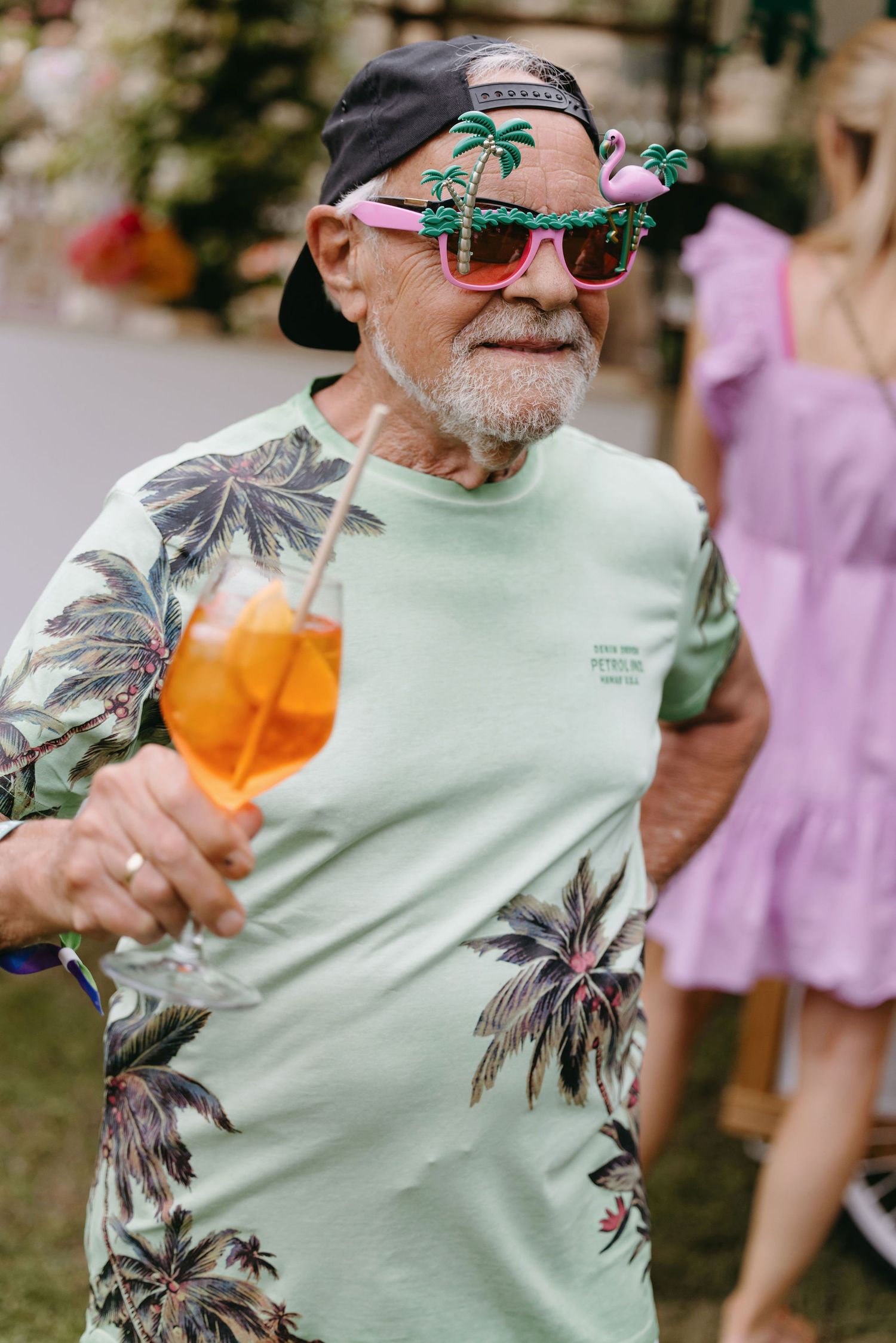 Guest wearing a tropical print shirt and sunglasses enjoying a drink at an outdoor event.