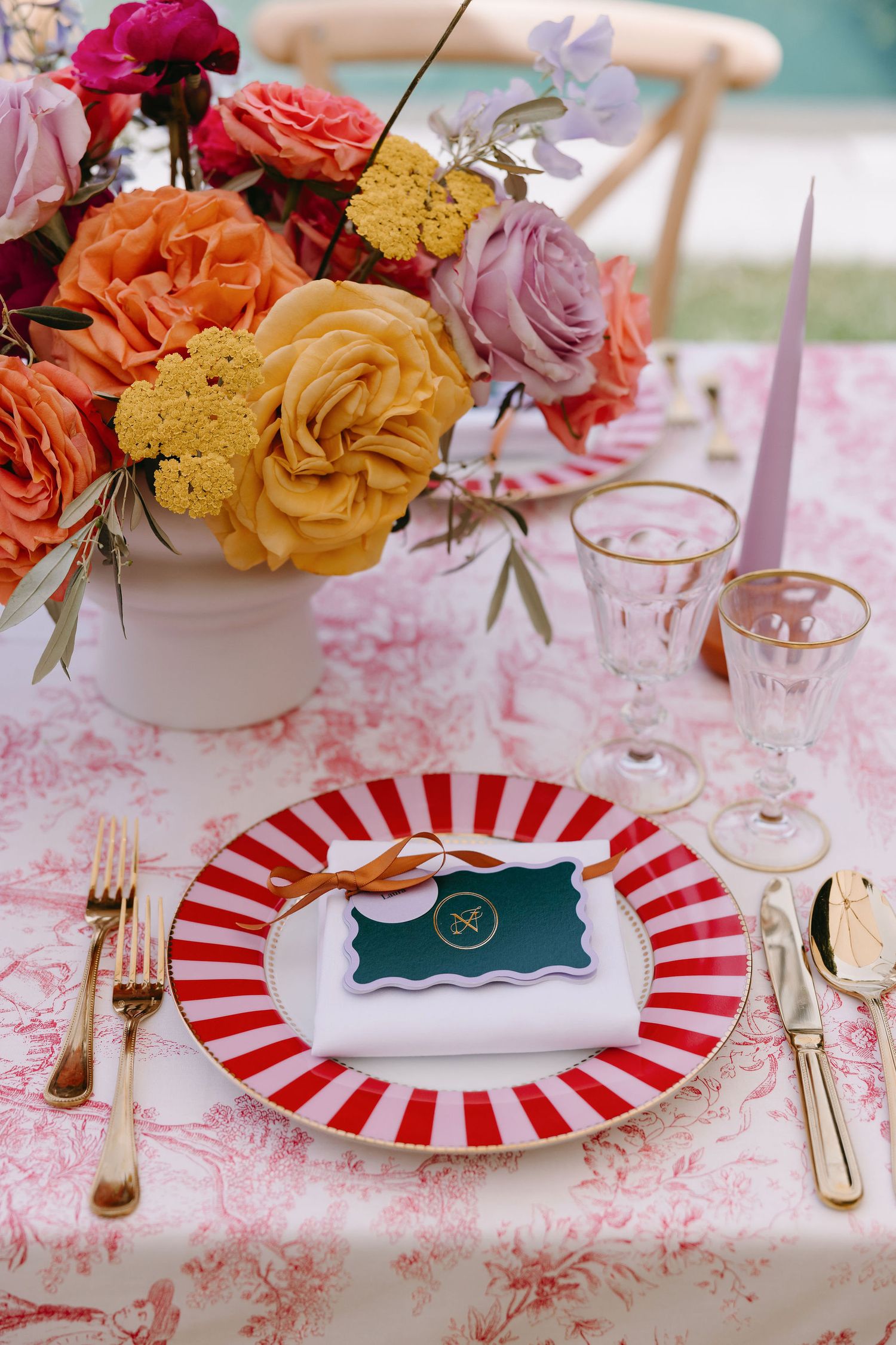 Colorful place setting with striped plate and vibrant rose centerpiece.