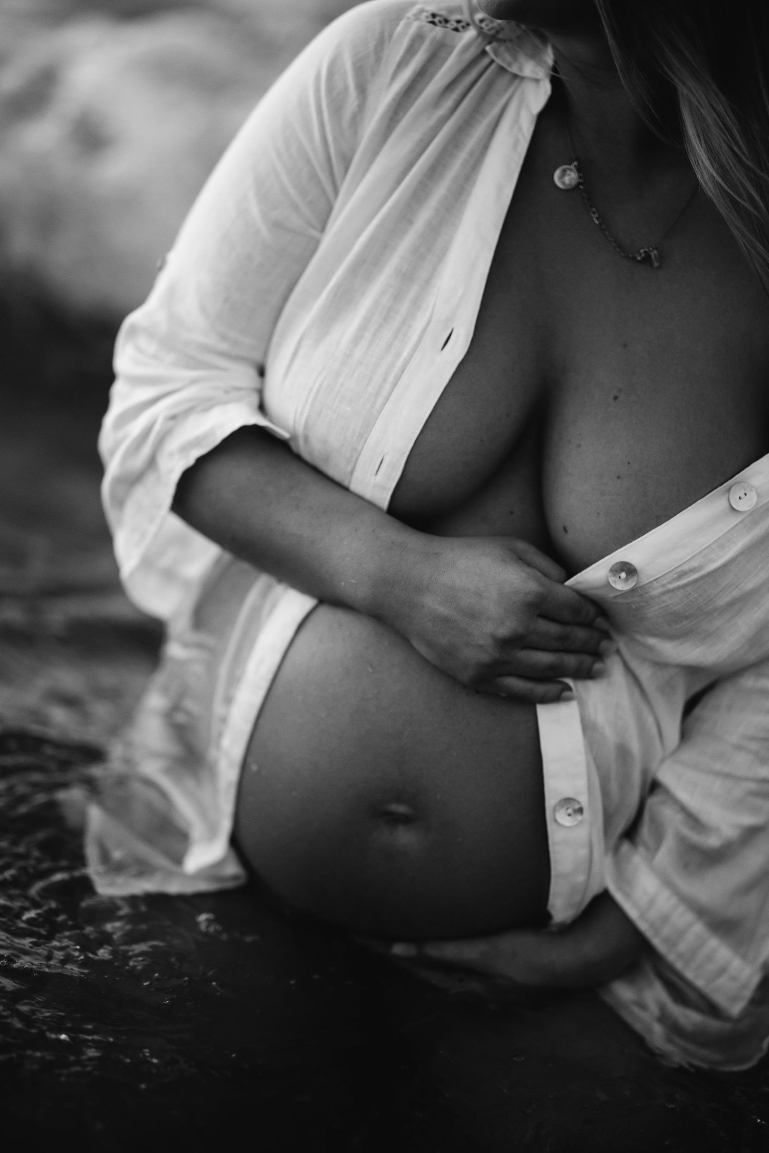 A black and white artistic photograph of an open white button-down shirt against a dark textured background.