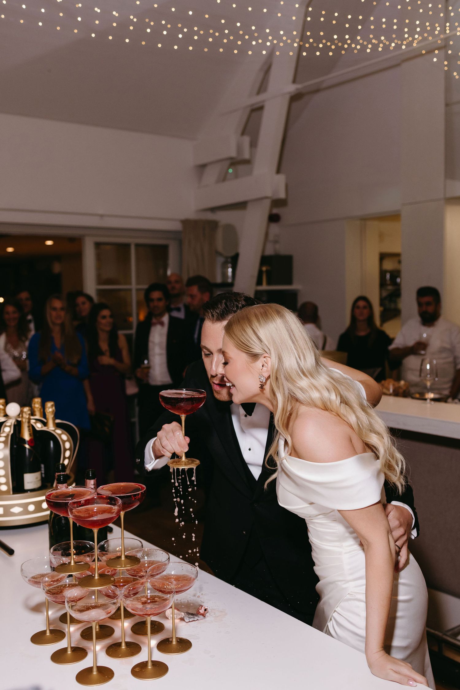 Wedding celebration featuring a champagne tower with multiple glasses being filled at an elegant reception.