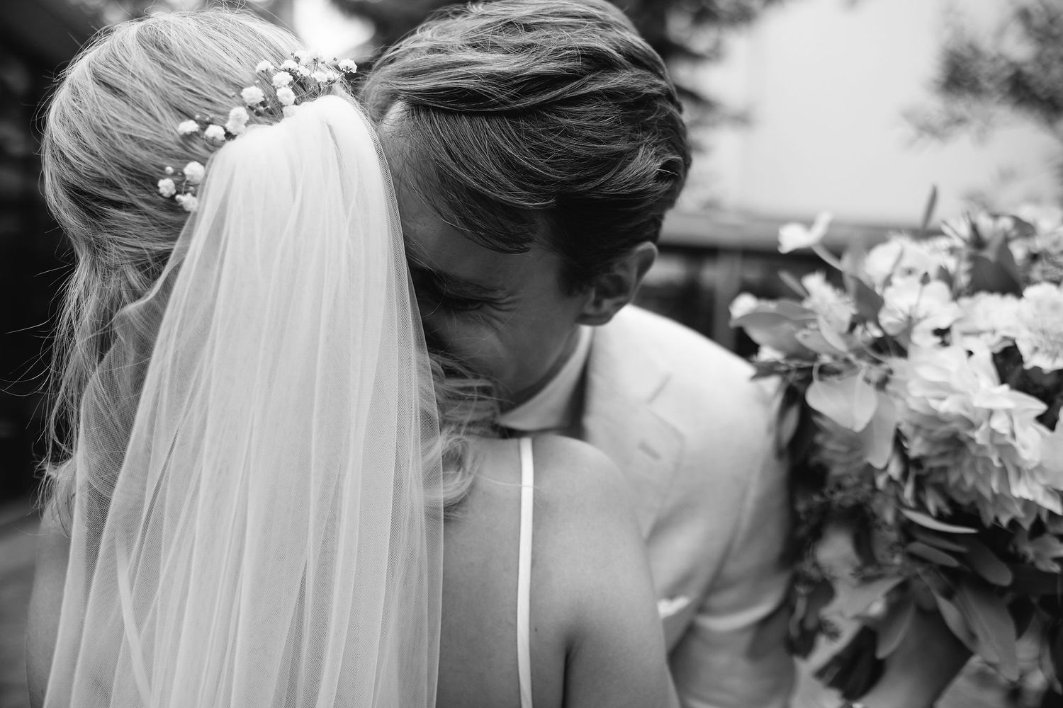 A tender black and white wedding moment captured with a flowing veil and floral bouquet.