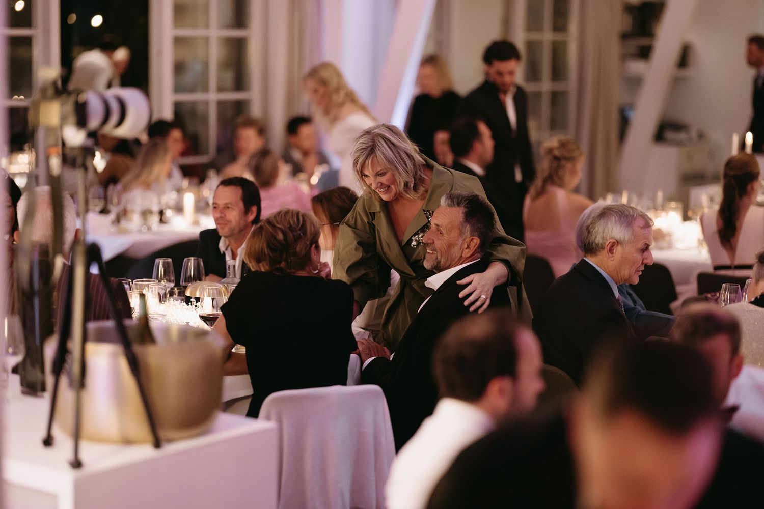 Elegant wedding reception guests enjoying dinner at tables with white linens and candlelight.