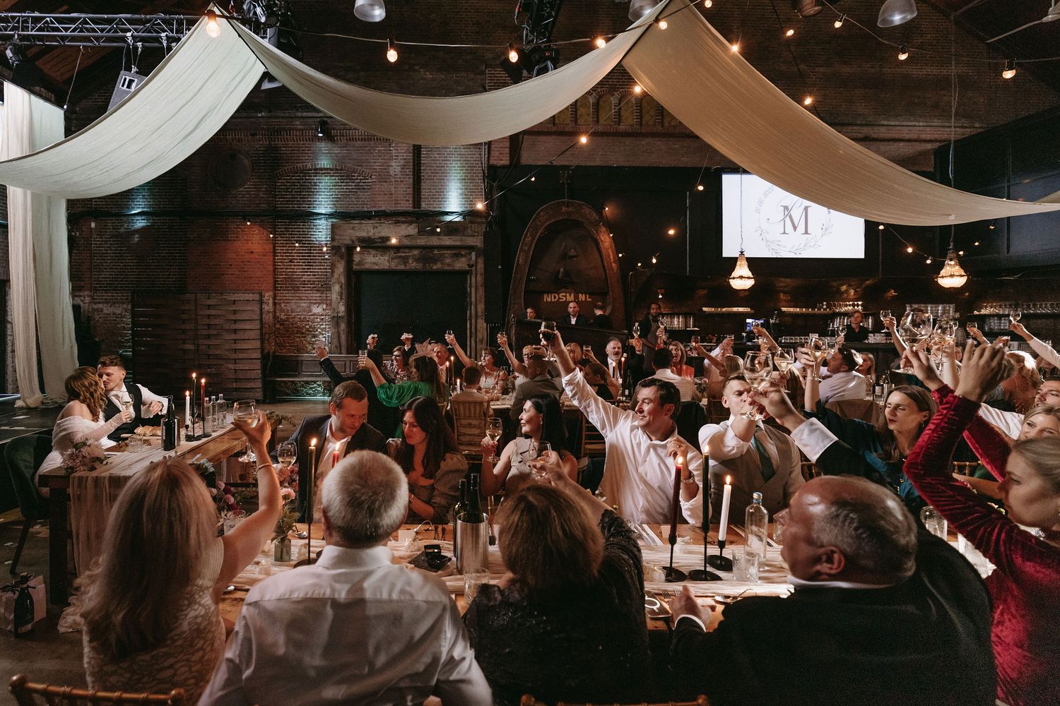 A crowded wedding reception venue with guests enjoying the celebration under draped fabric decor.