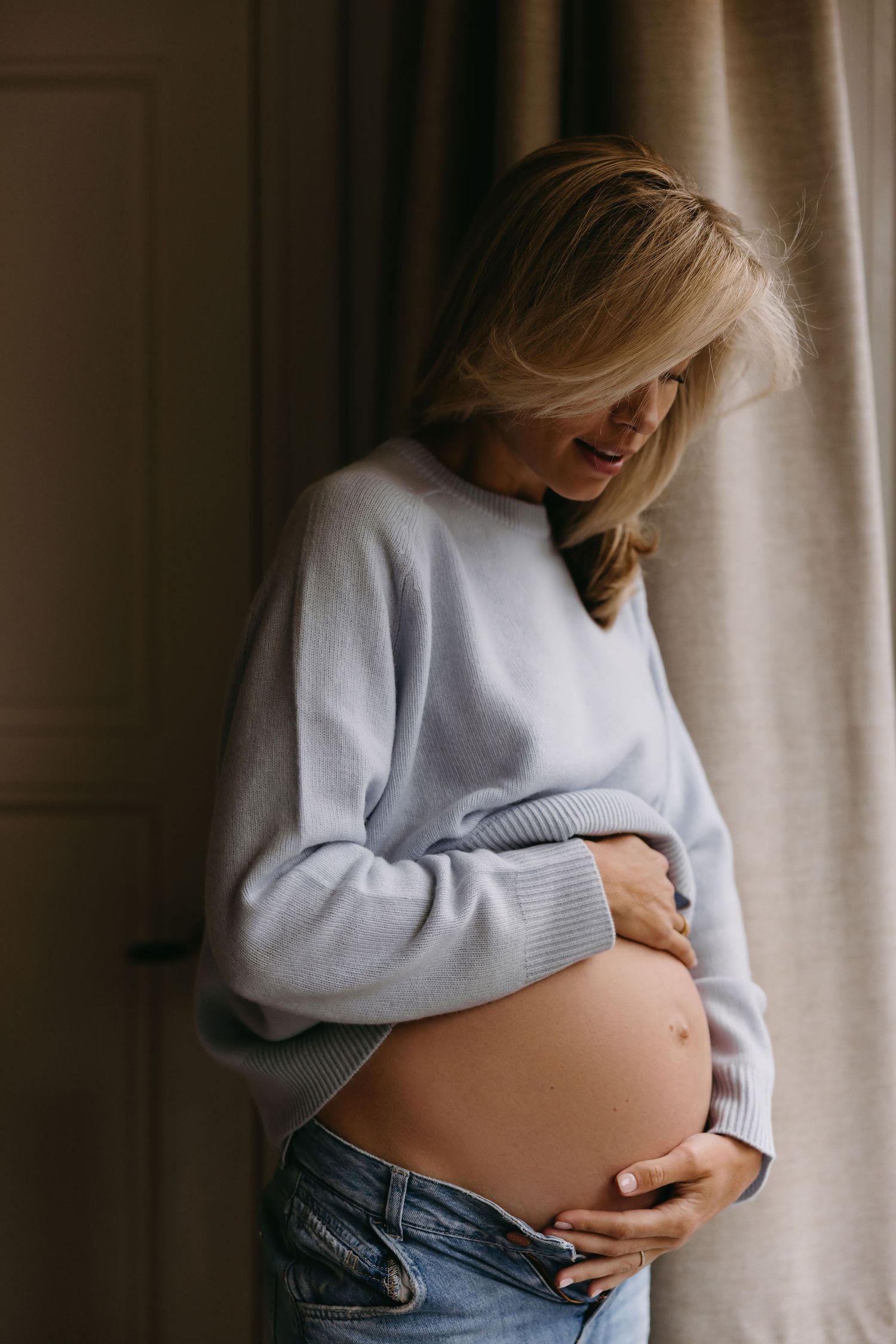Candid maternity photo showing baby bump in light blue sweater and jeans.
