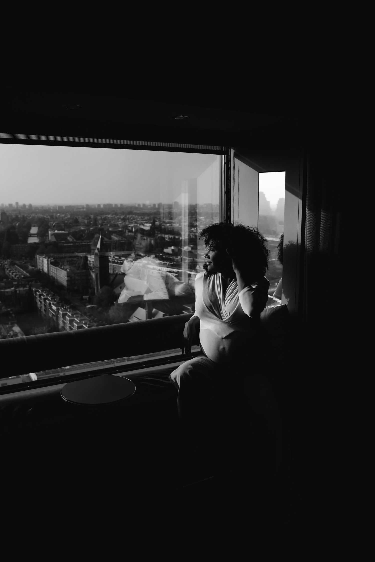 A silhouette against a large window overlooks a cityscape in dramatic black and white composition.