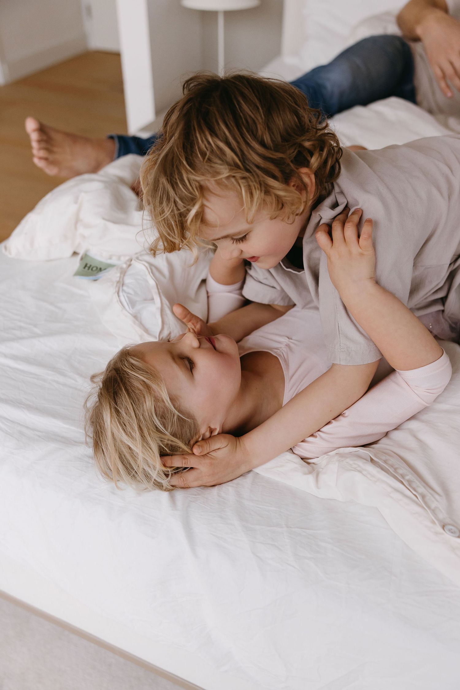 Documentary style photos show intimate family moments on crisp white bedding.