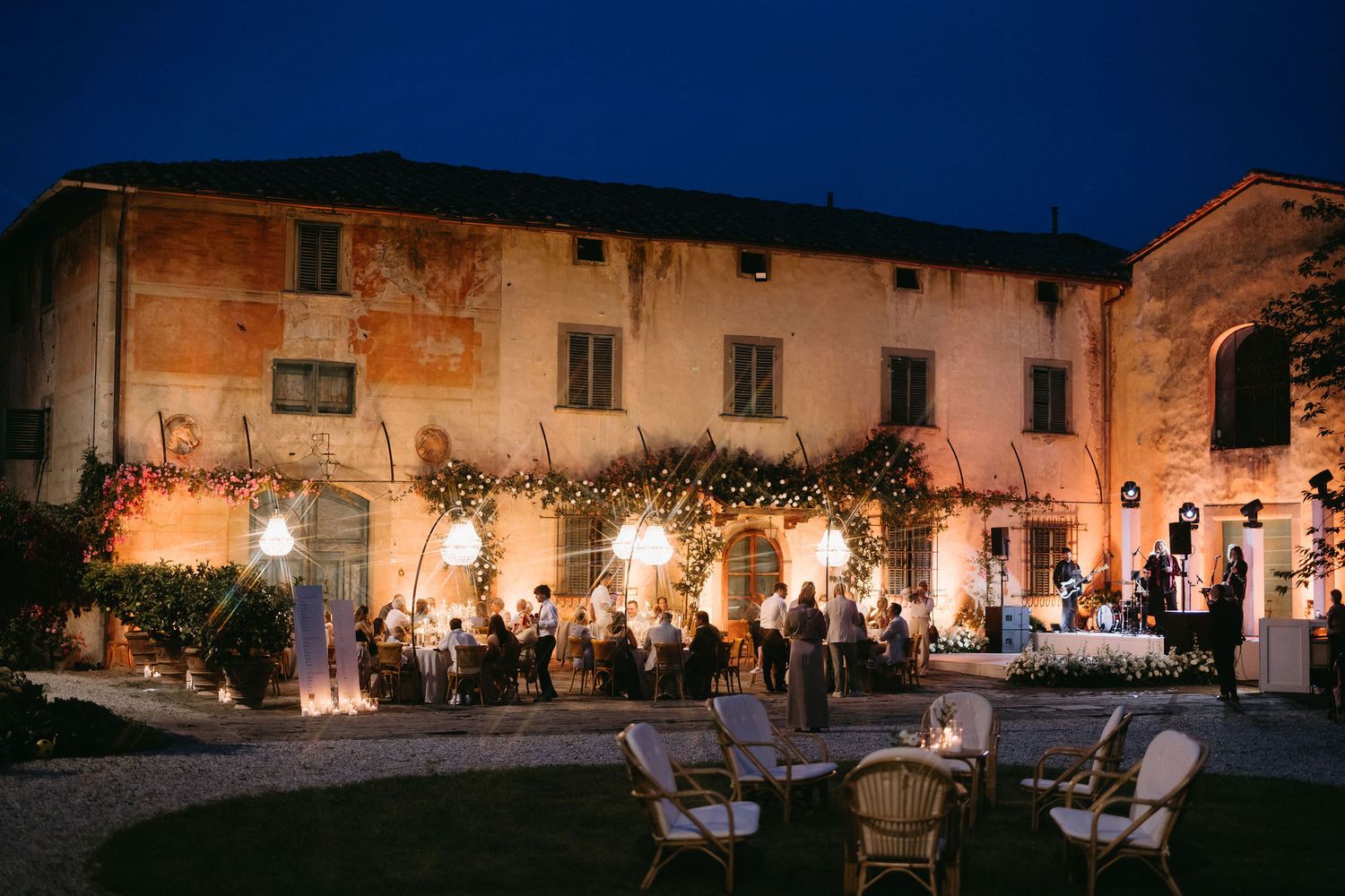 Outdoor evening reception at a rustic Italian villa illuminated by warm lighting and string lights.