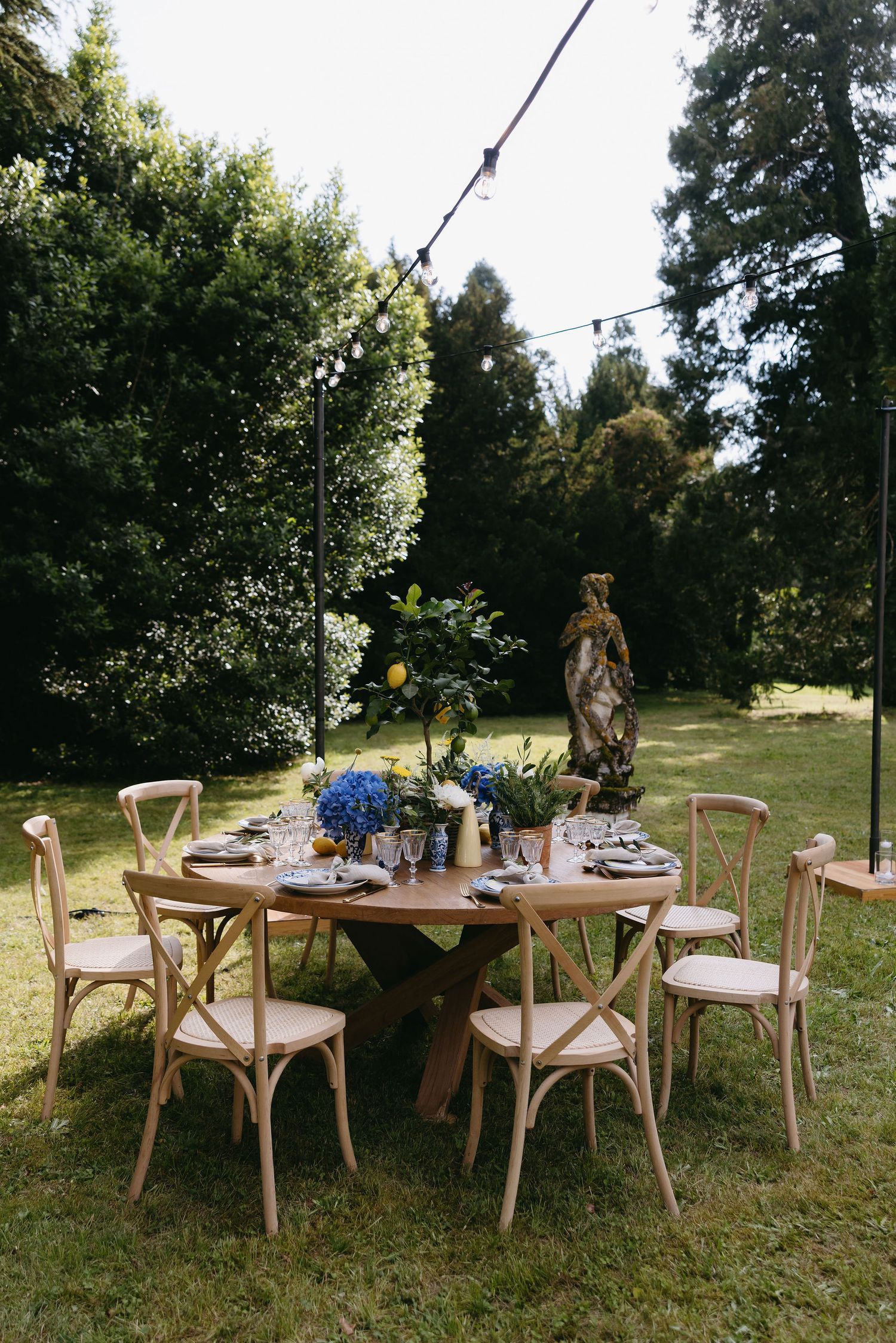 Garden party table setting with wooden chairs and string lights overhead.