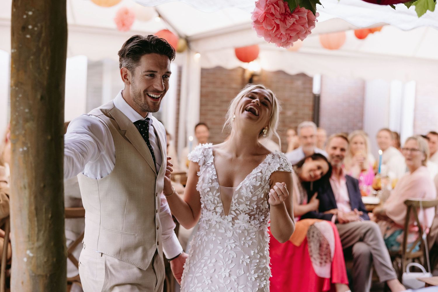 Joyful moment captured during wedding reception under tent with pink lanterns.