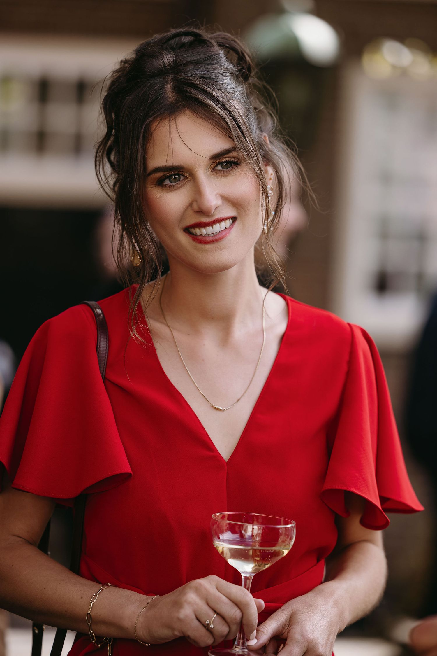 Person in red dress holding wine glass and smiling warmly.