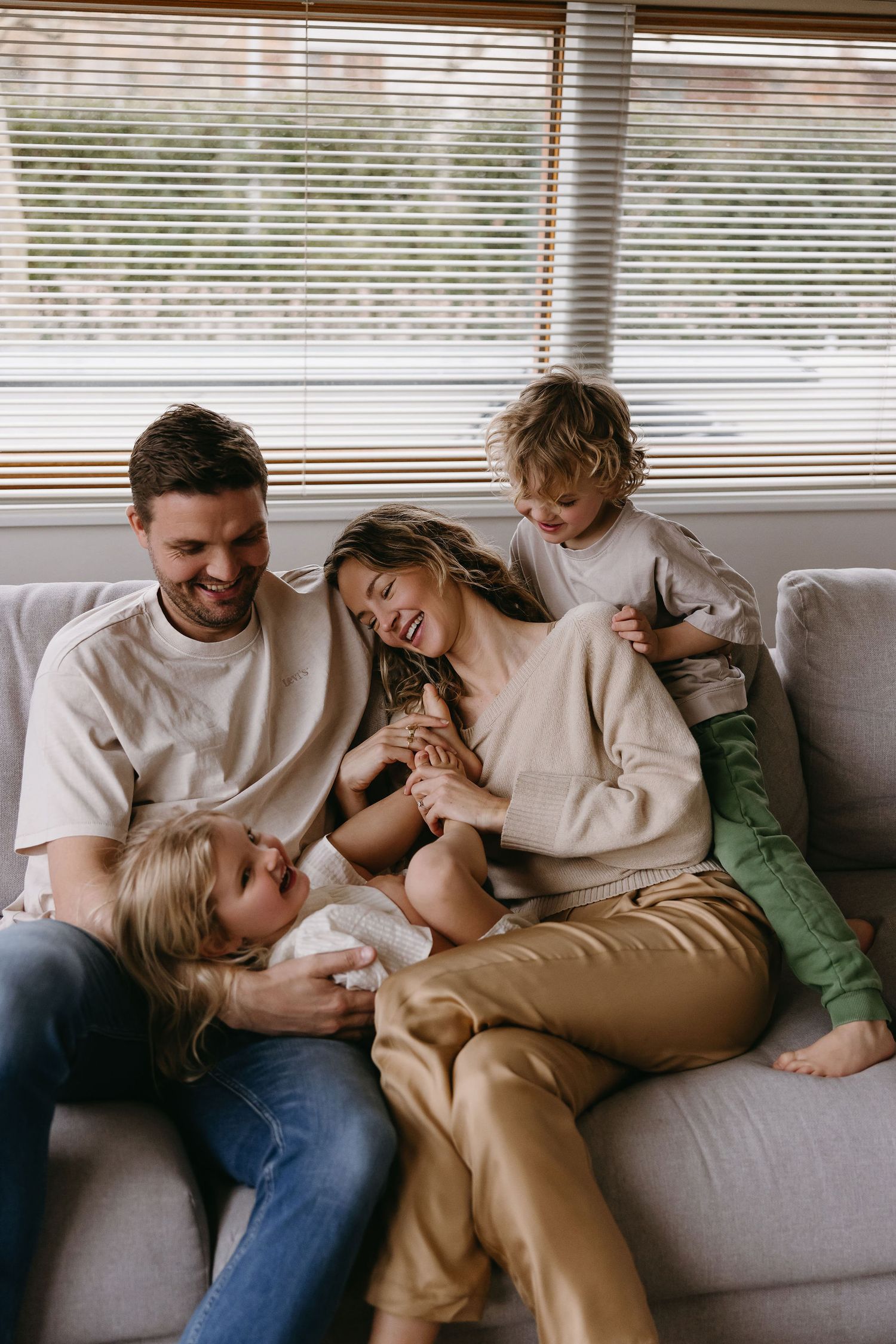 Candid black and white photos show tender moments of family cuddles on a cozy sofa.