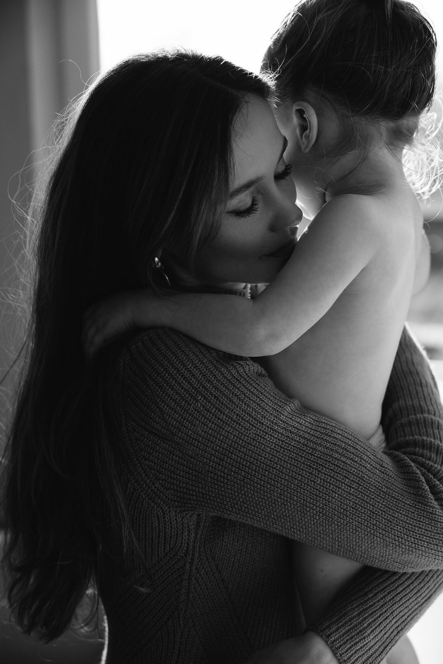 An intimate black and white portrait capturing a tender embrace in soft lighting.