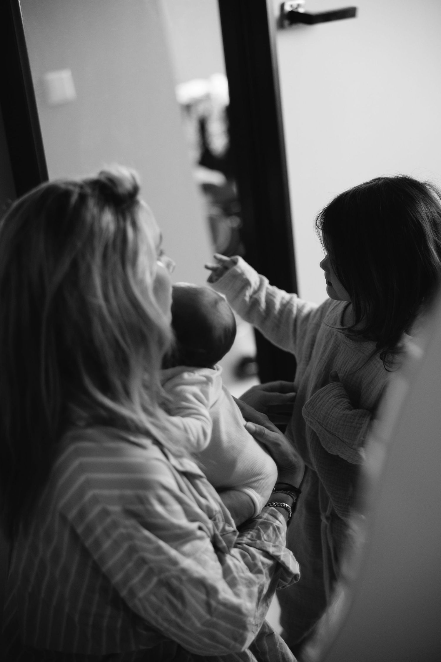 A black and white candid moment of family interaction with a baby.