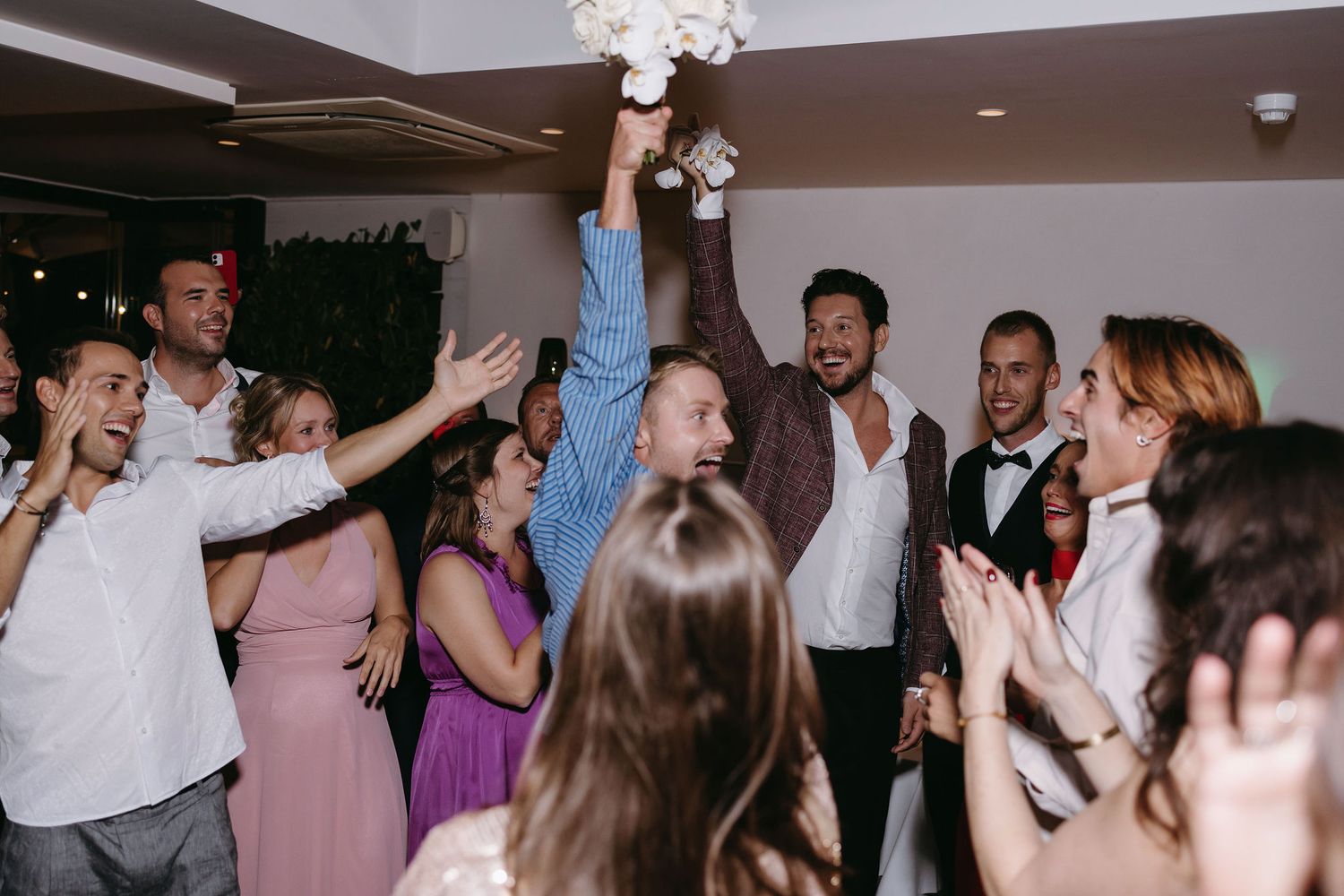 Dance party celebration on a wedding reception dance floor with people dancing under crystal chandeliers.