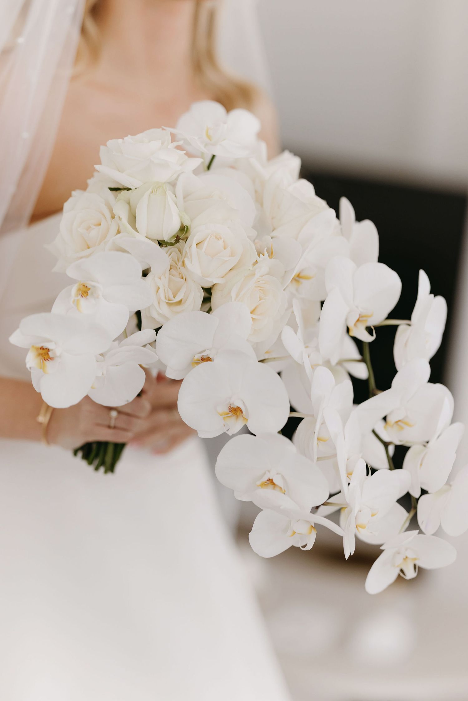 Close up of elegant white orchid bridal bouquet against light background.