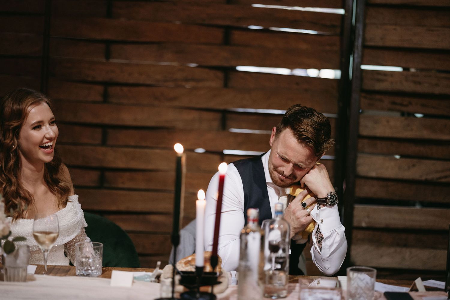 Wedding reception guests enjoying dinner and conversation at wooden tables.