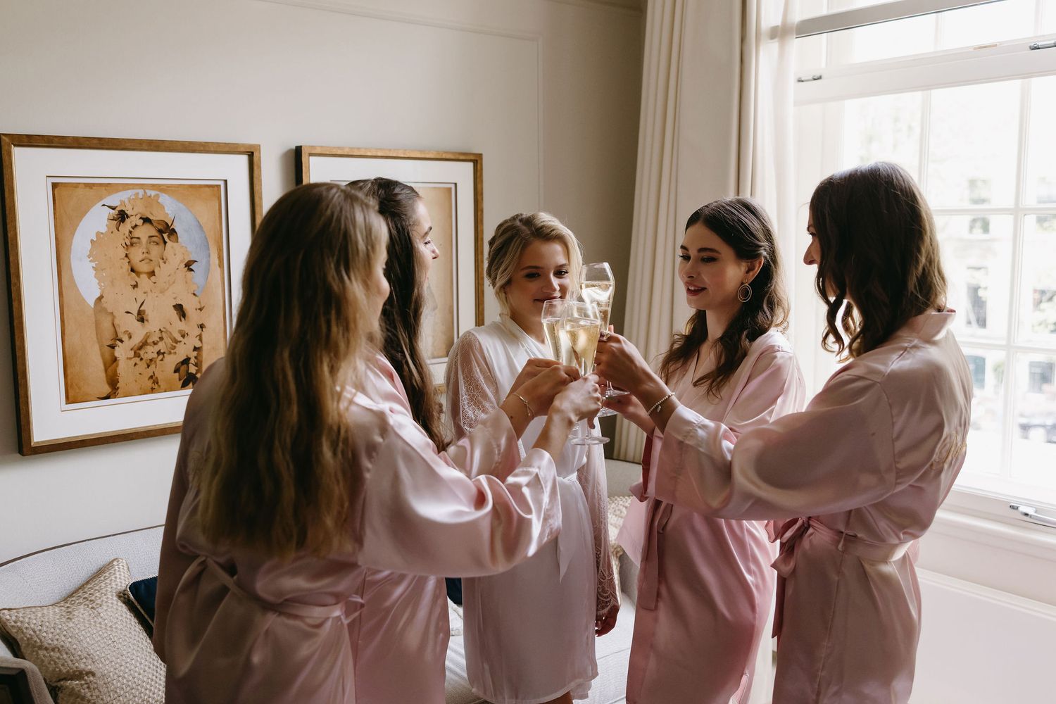 Group in pink robes toasting with champagne glasses by a bright window.