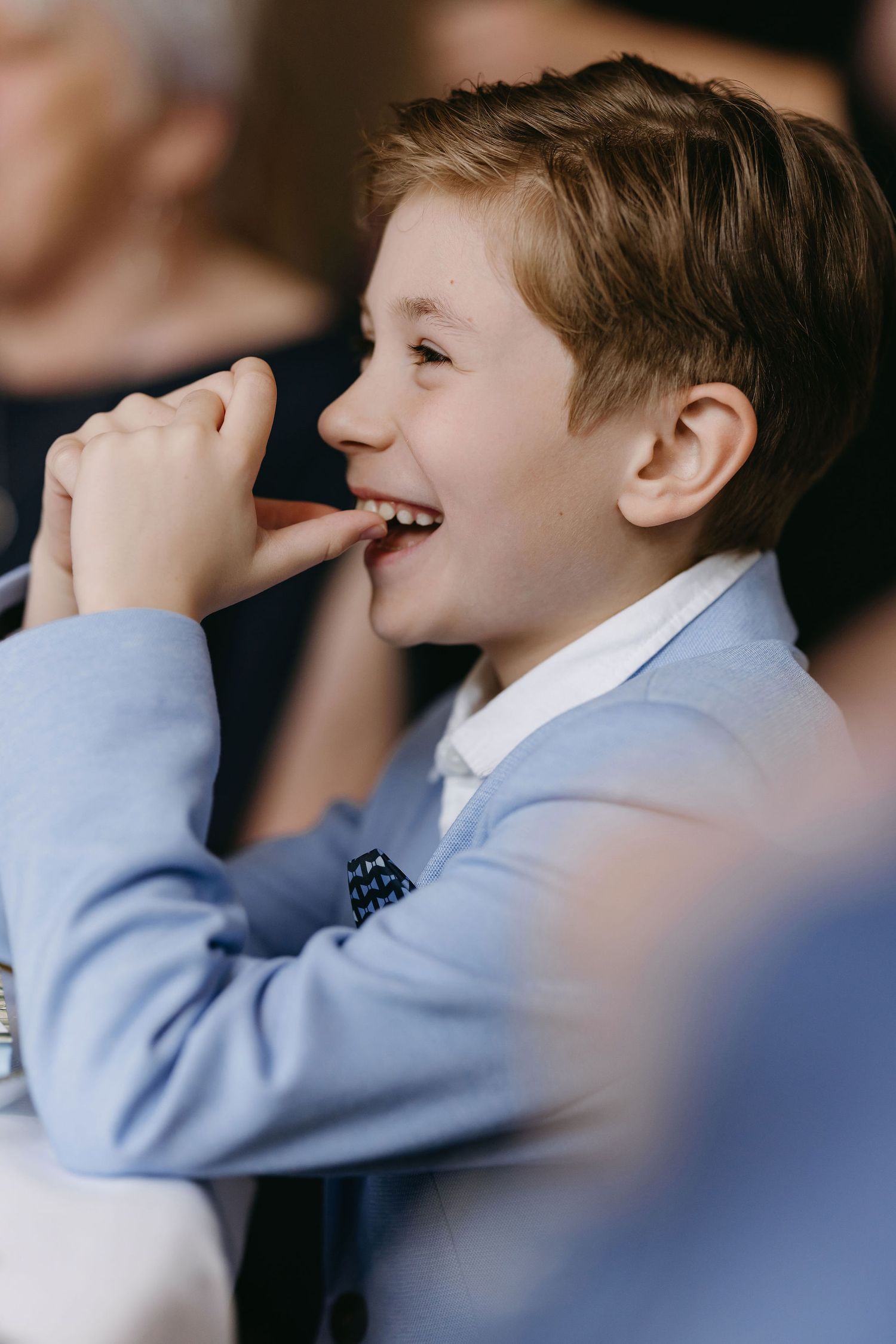 Young boy in light blue suit jacket smiling and laughing during a wedding celebration.