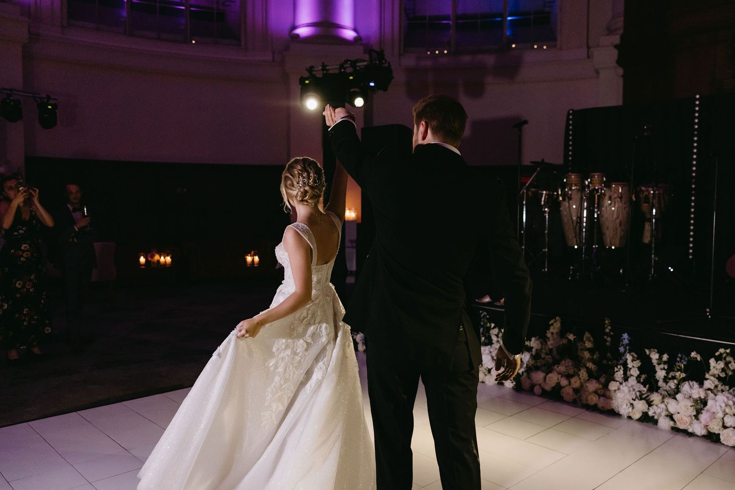 Elegant wedding reception dance floor lit with purple uplighting and string lights.