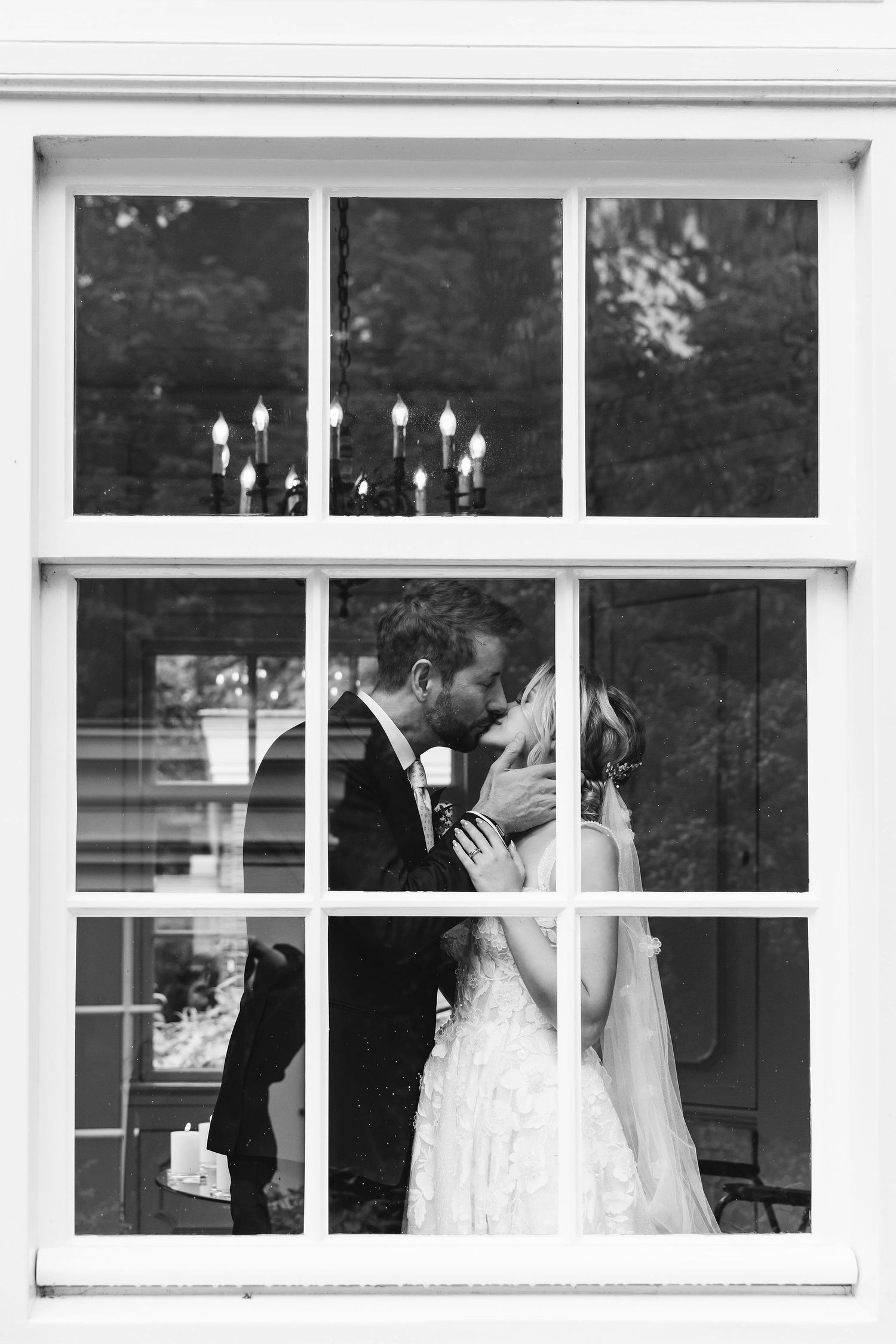 Wedding couple's romantic moment captured through window panes in black and white.