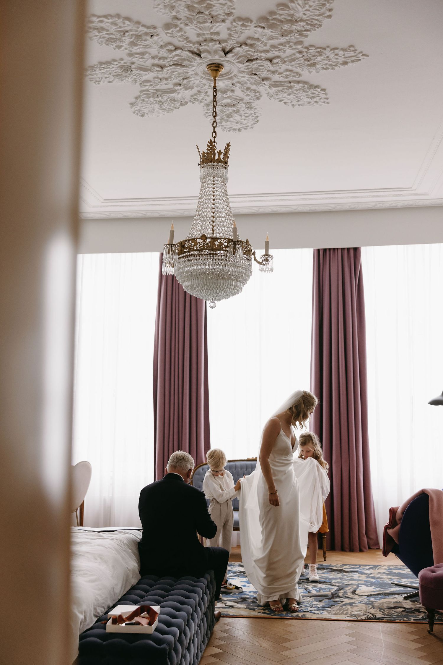 Elegant hotel room with ornate ceiling detail and pink curtains during wedding preparations.