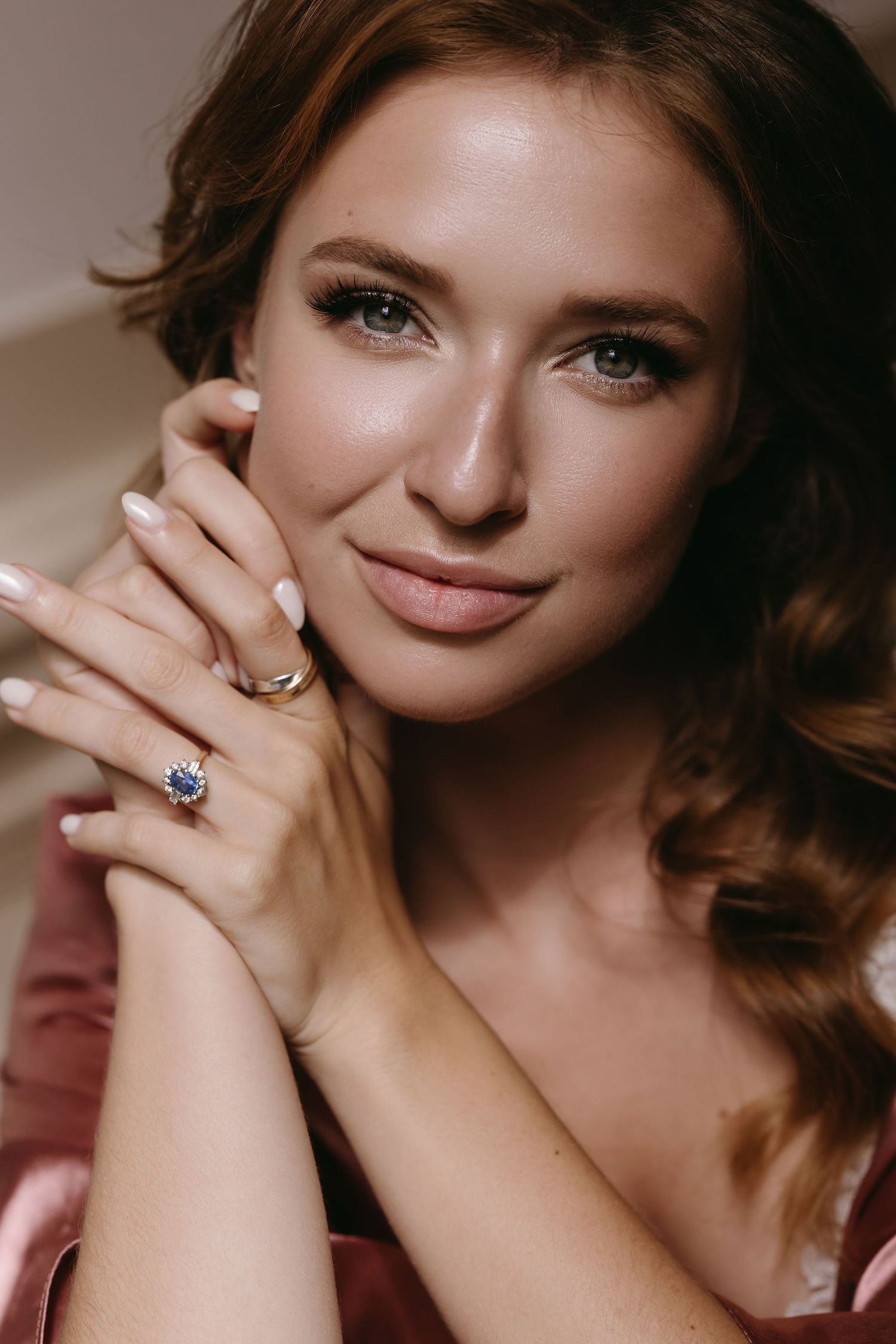 Close-up portrait with elegant jewelry featuring a blue gemstone ring and subtle makeup in warm lighting.
