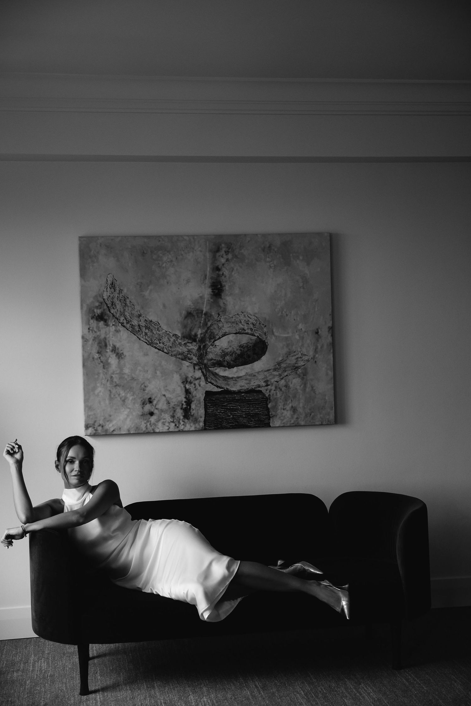 A dramatic black and white series of someone lying motionless on a dark couch beneath abstract wall art.