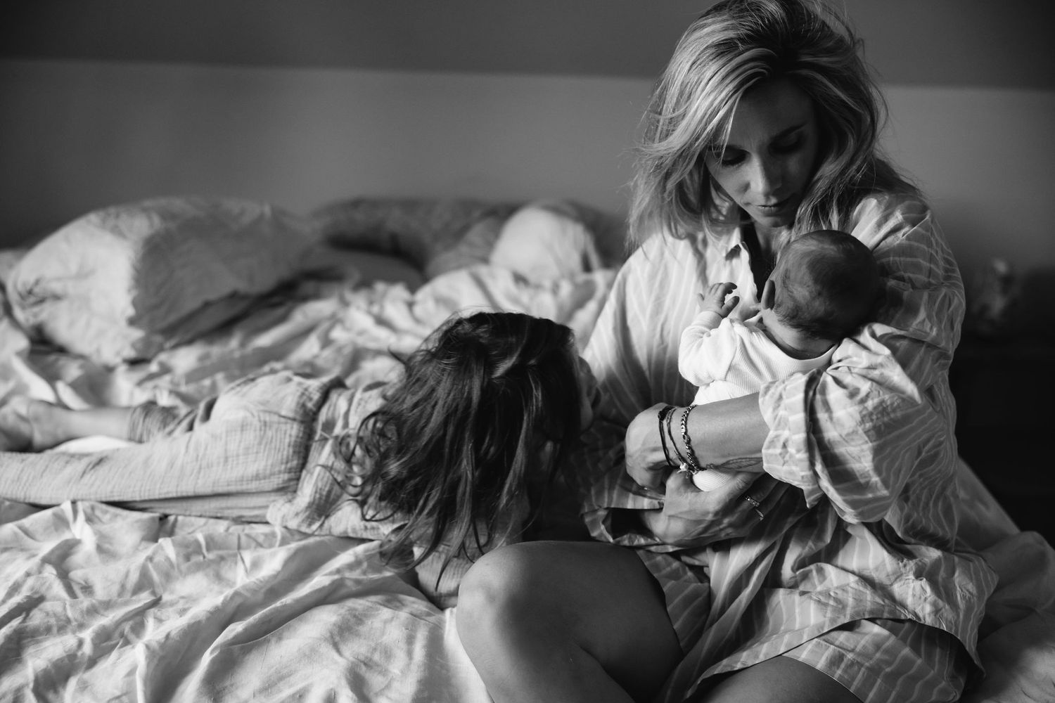 Black and white photograph of family sharing intimate moments on a bed.