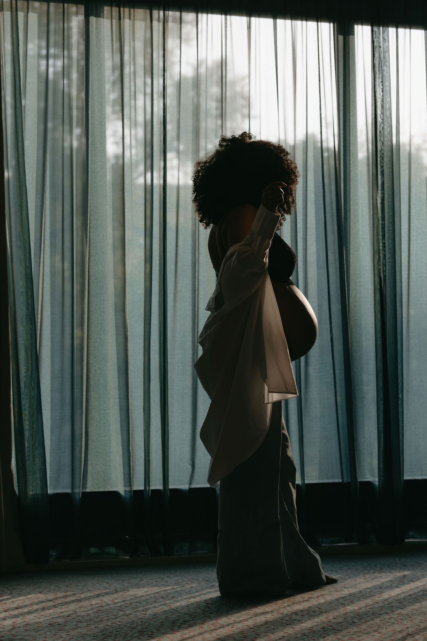 Silhouette stands against sheer curtains in moody natural lighting.