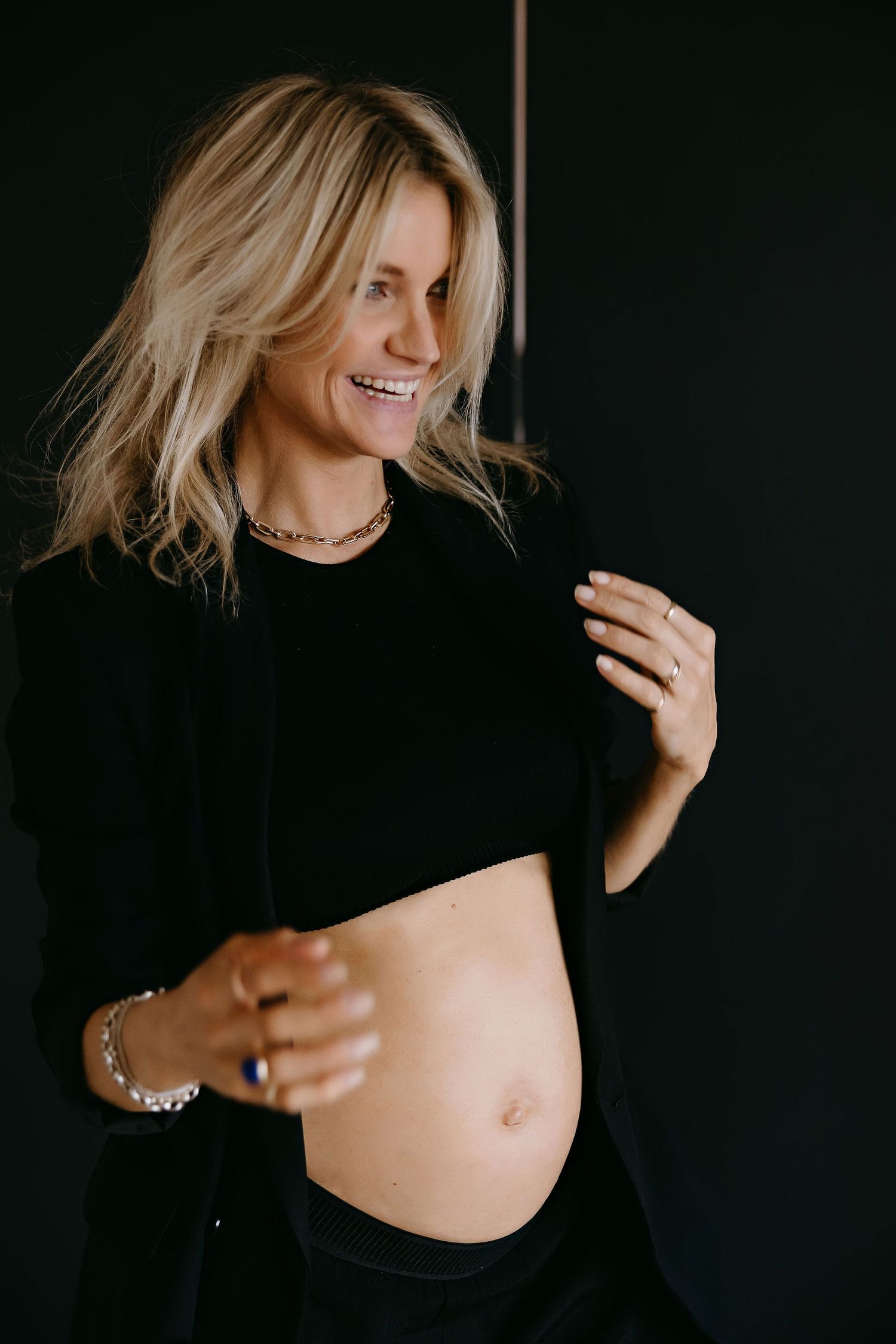 A pregnancy photo shows a woman in black clothing smiling while revealing her baby bump.