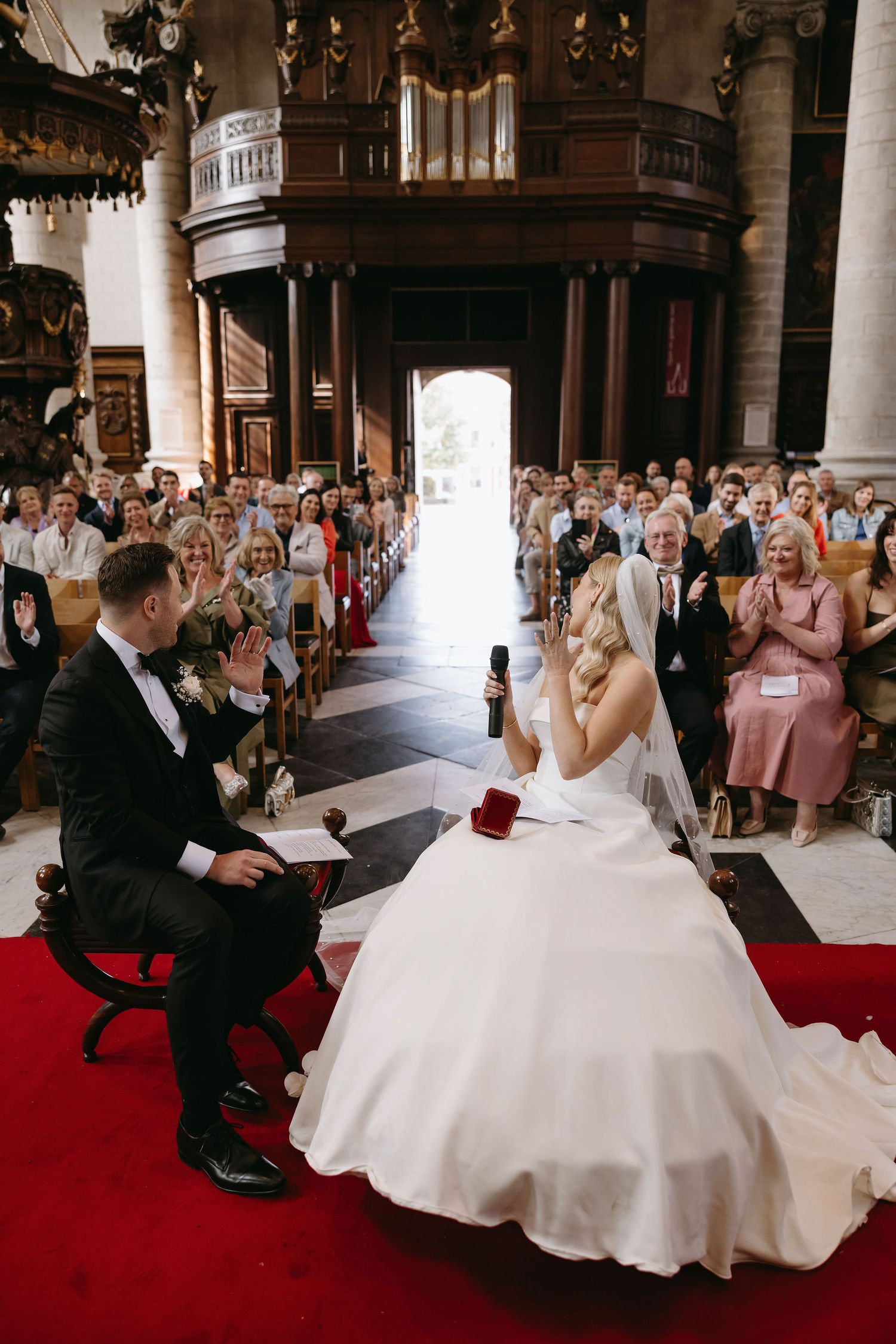 Wedding ceremony in an ornate church with red carpet and marble columns.