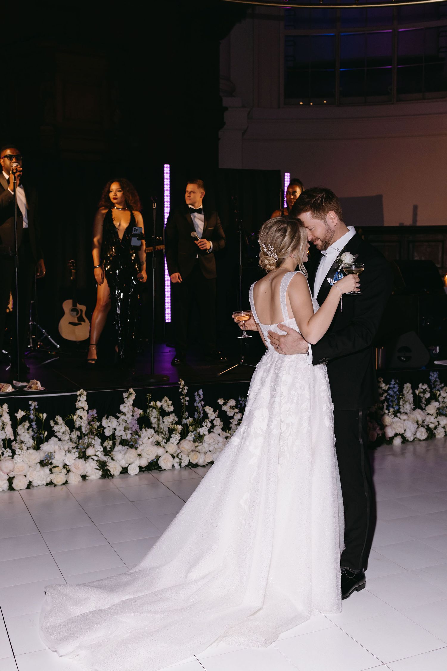 Romantic first dance at a wedding with band performing in the background and white floral decorations.