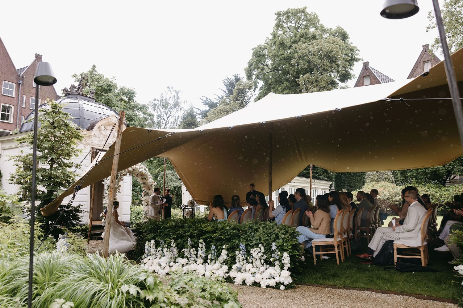 An outdoor wedding reception under a stretched tent canopy with white floral decorations.