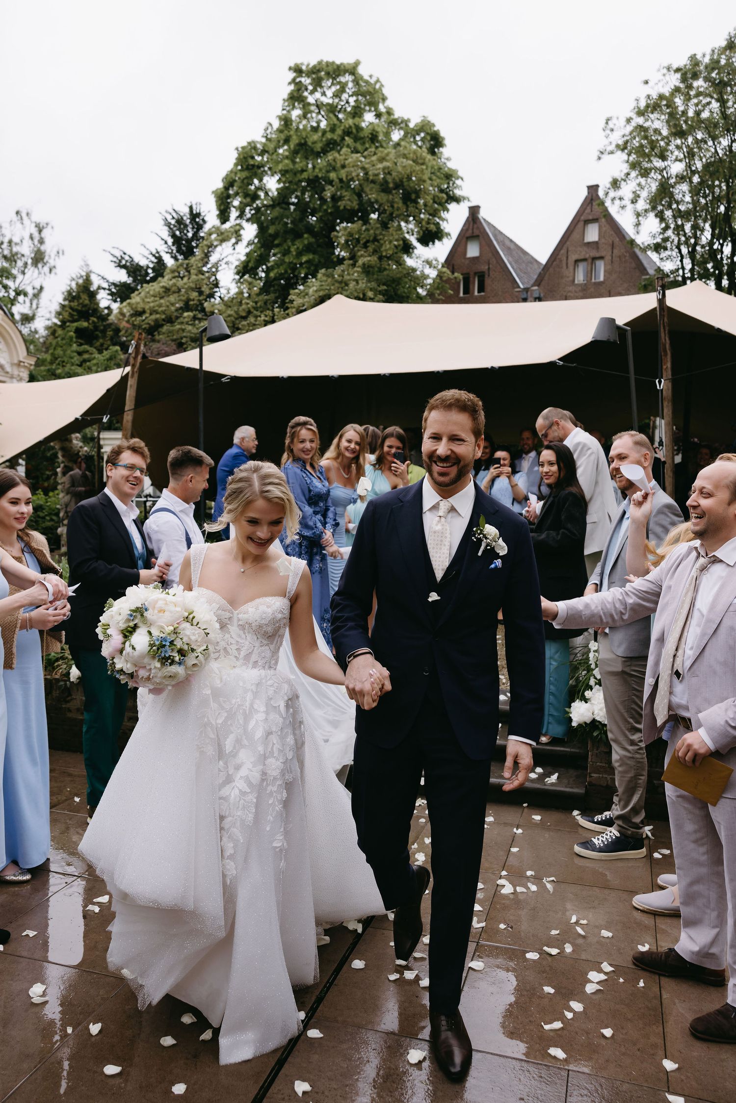 Wedding party celebrating outdoors with confetti and laughter under fabric canopies.