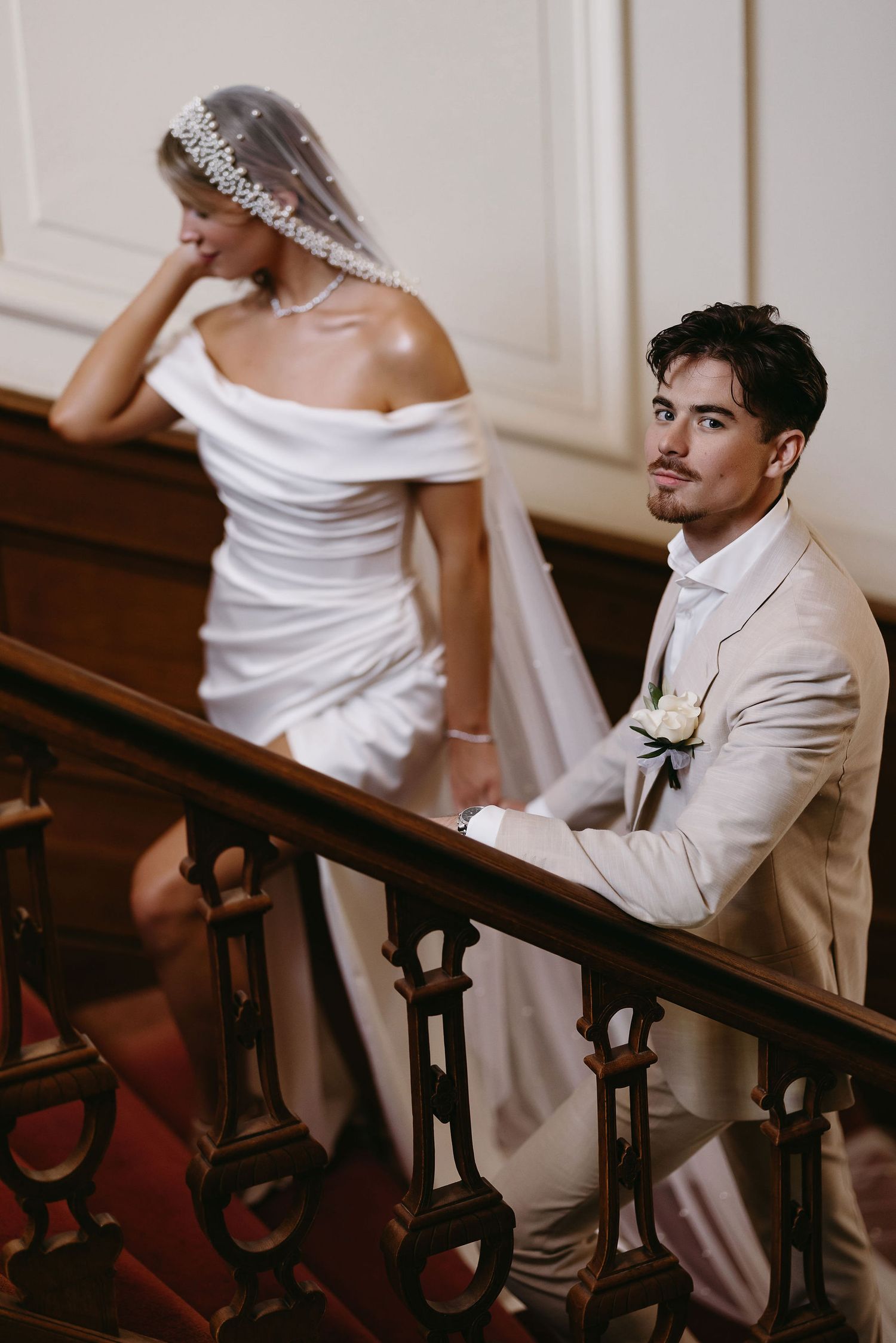 An intimate wedding moment captured on ornate stairs with light and shadow playing across formal attire.