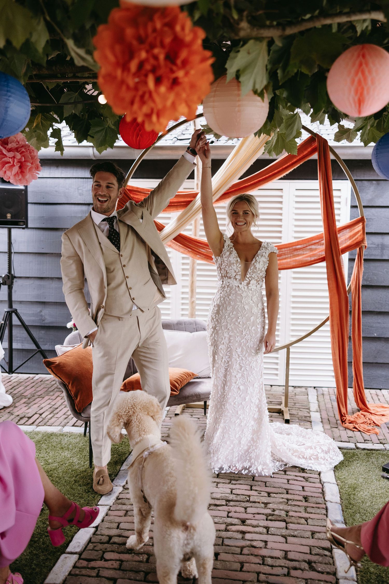 A white fluffy dog joins a celebratory moment under coral-colored decorations on a brick patio.