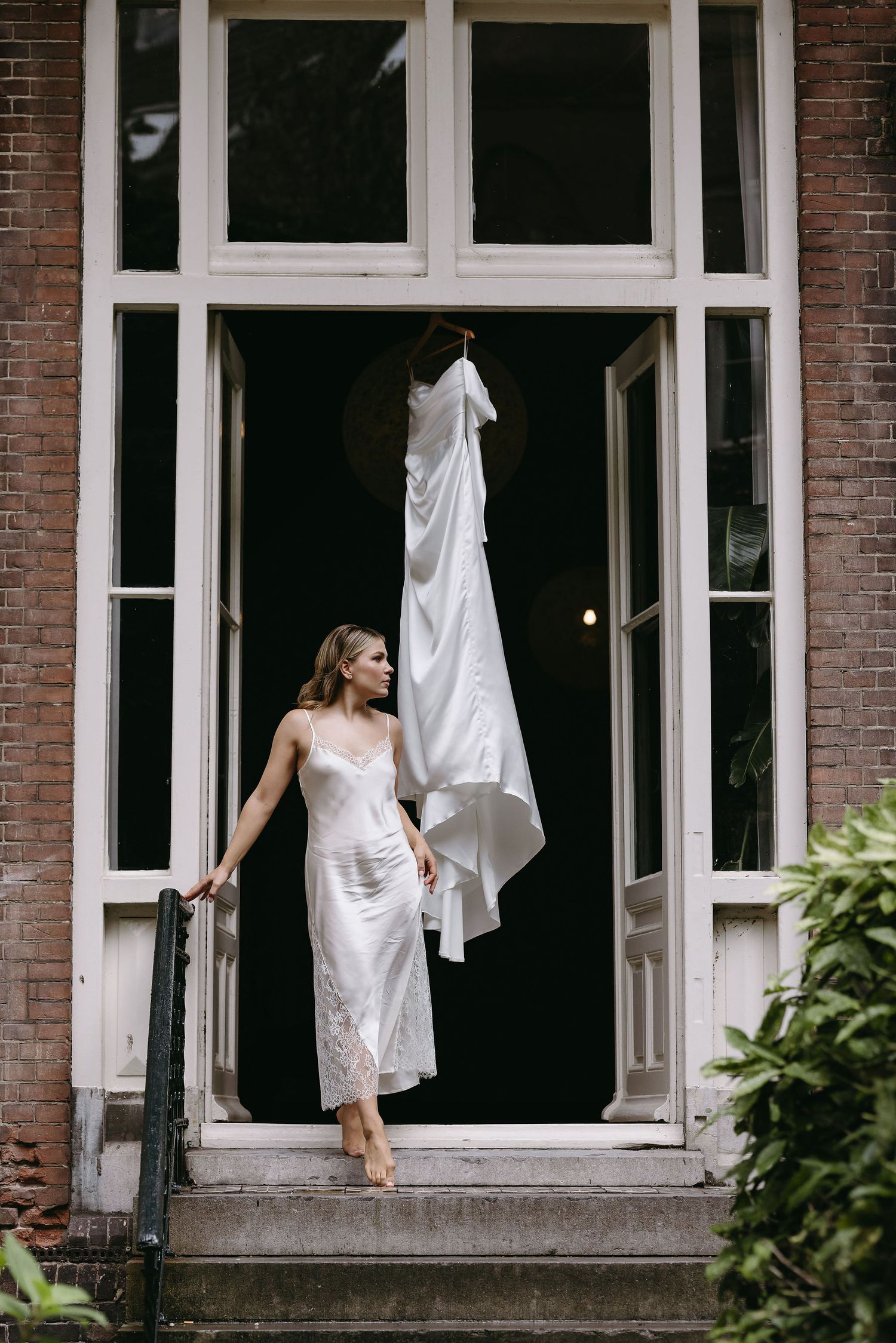 Sequence of bride in white dress on steps of brick building with large windows.