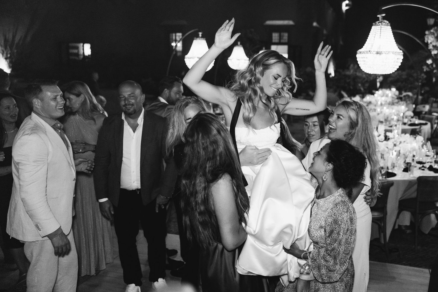 Wedding celebration scene with guests dancing and celebrating in black and white.